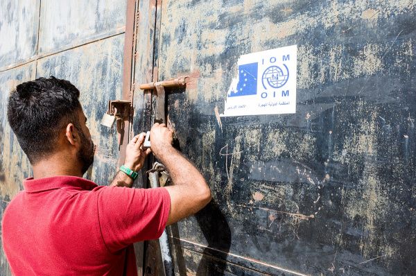 A guard at the Nasr detention center in Zawiya opens a prison door that boasts a sticker from the European Union and IOM. Image by Peter Tinti. Libya, 2017.