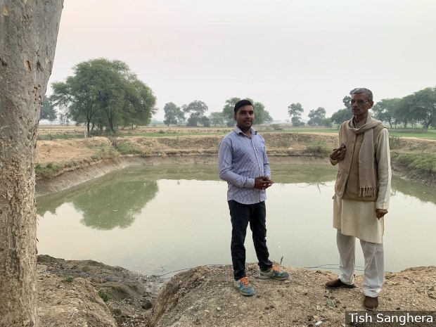Nawal Kishore Diwedi (on right) with his son-in-law, Vedprakash Diwedi, in front of a pond built under the ‘Khet Talab Yojana’, or ‘Farm Pond Scheme’. They no longer struggle to irrigate their fields and have observed a rise in groundwater levels. Image by Tish Sanghera. India, undated. 

