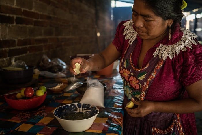 Victoria Santiago Lopez, 35, from San Miguel del Valle in Oaxaca, prepares lunch. She squeezes a lemon from her garden into boiled green beans, and mixes tomatillo (Mexican husk tomato) and other ingredients into fresh tomatillo salsa, a traditional Zapotec recipe. All the ingredients are locally grown. Image by James Whitlow Delano. Mexico, 2017.