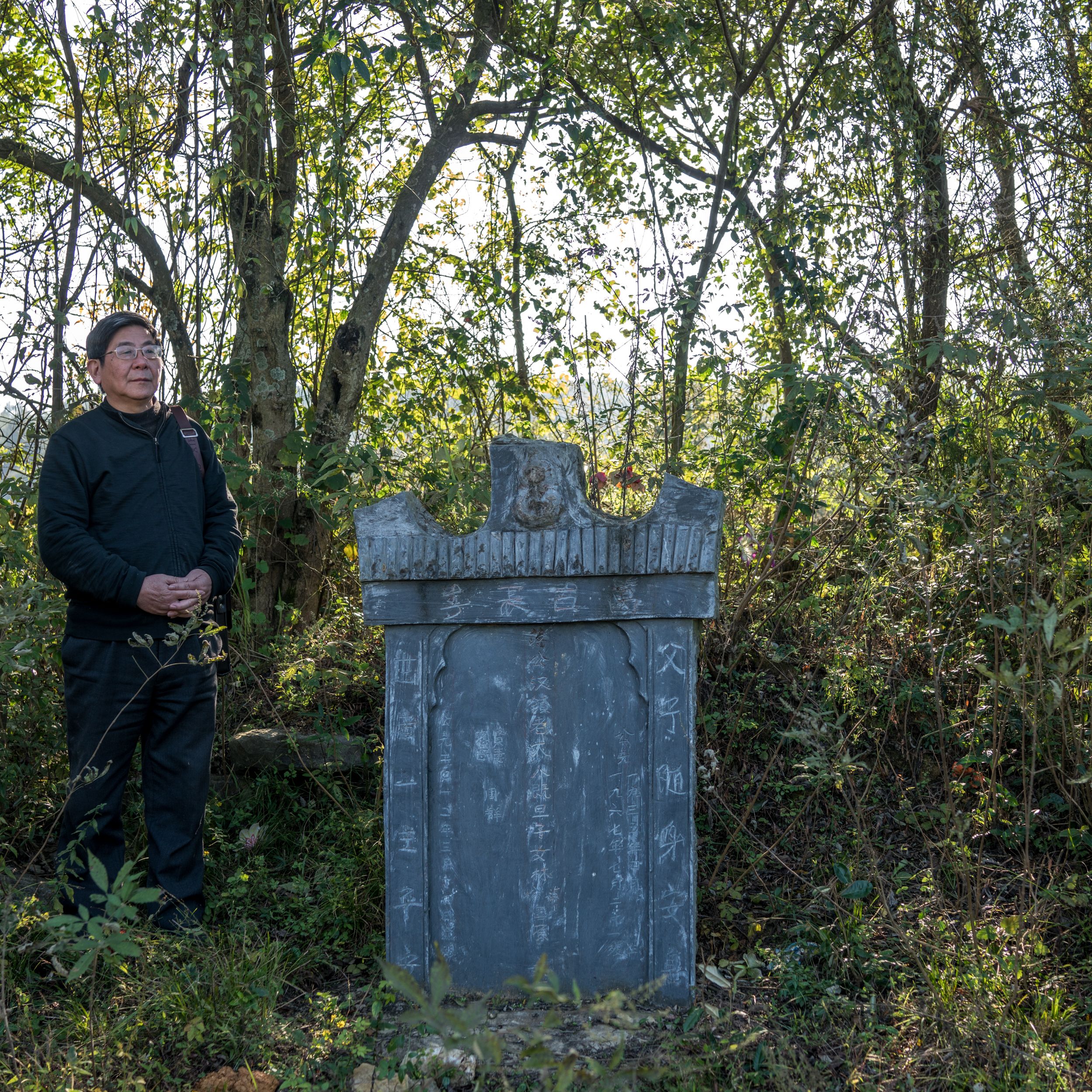 Tan Hecheng at a tombstone put up by Zhou Qun for her husband and three children, who were among the thousands of people killed during the Cultural Revolution in Dao County. Image by Sim Chi Yin. China/VII, 2016.