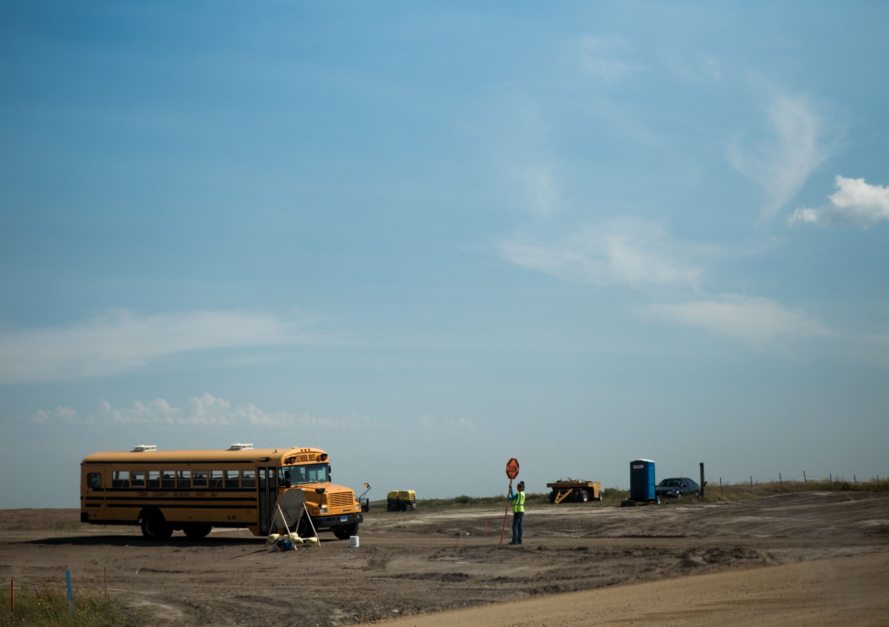 A bus takes children home after school alongside a developing road on August 30, 2018, after school on the Rosebud Indian Reservation in rural South Dakota. Image by Brian Munoz. South Dakota, 2018.