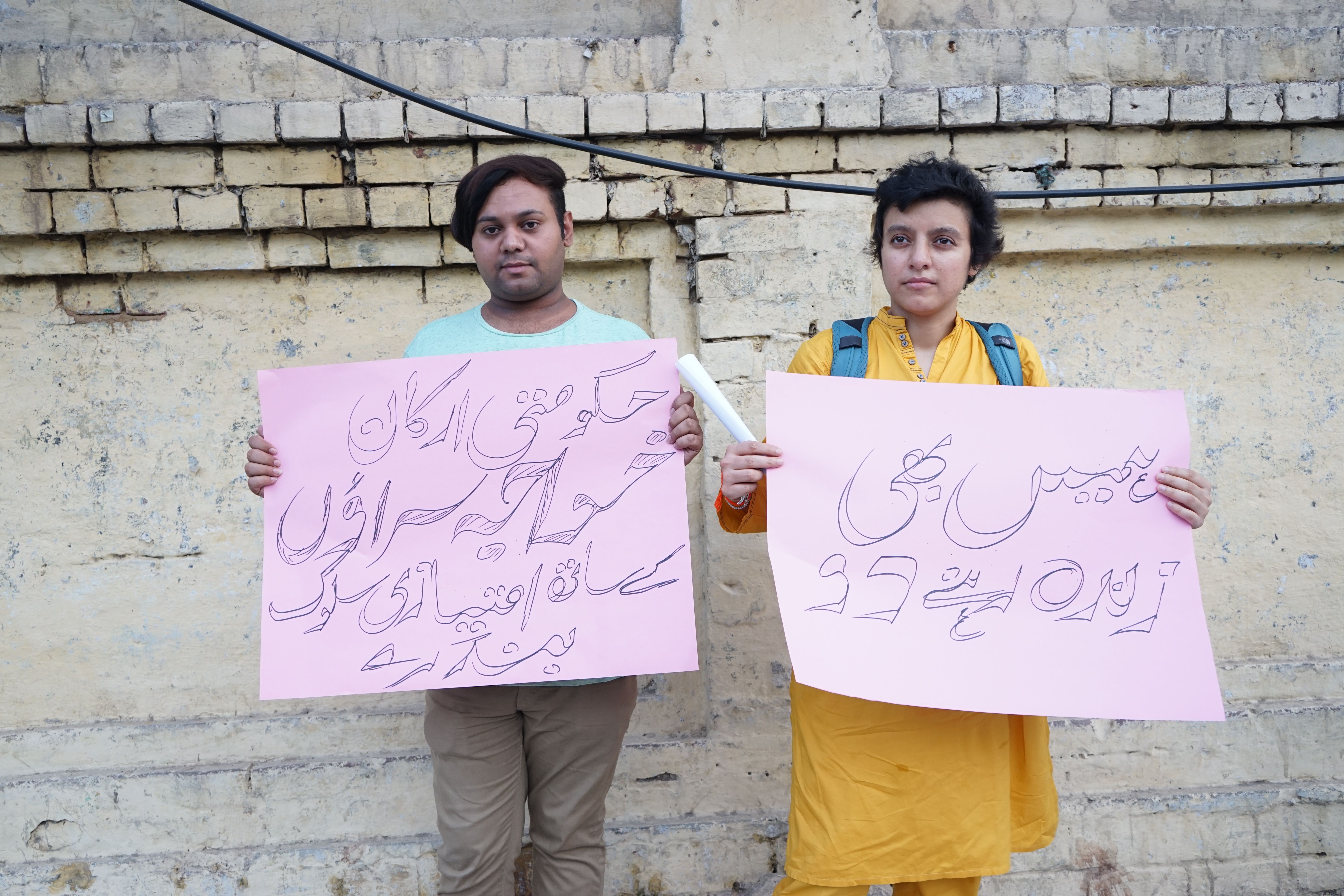 Two protesters, Sara and Sunny, holding signs in solidarity with the khawaja sira community.  Signs right to left read: "Let us live, too" and  "Government members, stop discriminating against khawaja siras." Image by Ikra Javed. Pakistan, 2016.