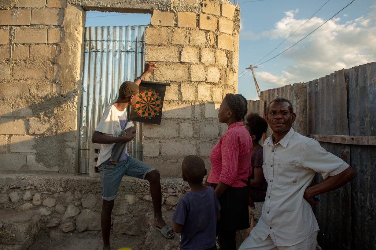 Alisma Robert, right, and children Esaie Robert, 15, Roberson Robert, 7, and Kerline Reobert, 18, standing, enjoy the evening at their home in the Canaan 3 neighborhood of greater Canaan, Haiti, January 7. Thomson Reuters Foundation. Image by Allison Shelley. Haiti, 2019.