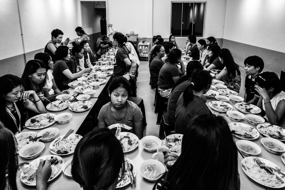Close to 40 men and women sit around a table and share a meal inside the kitchen of the shelter.