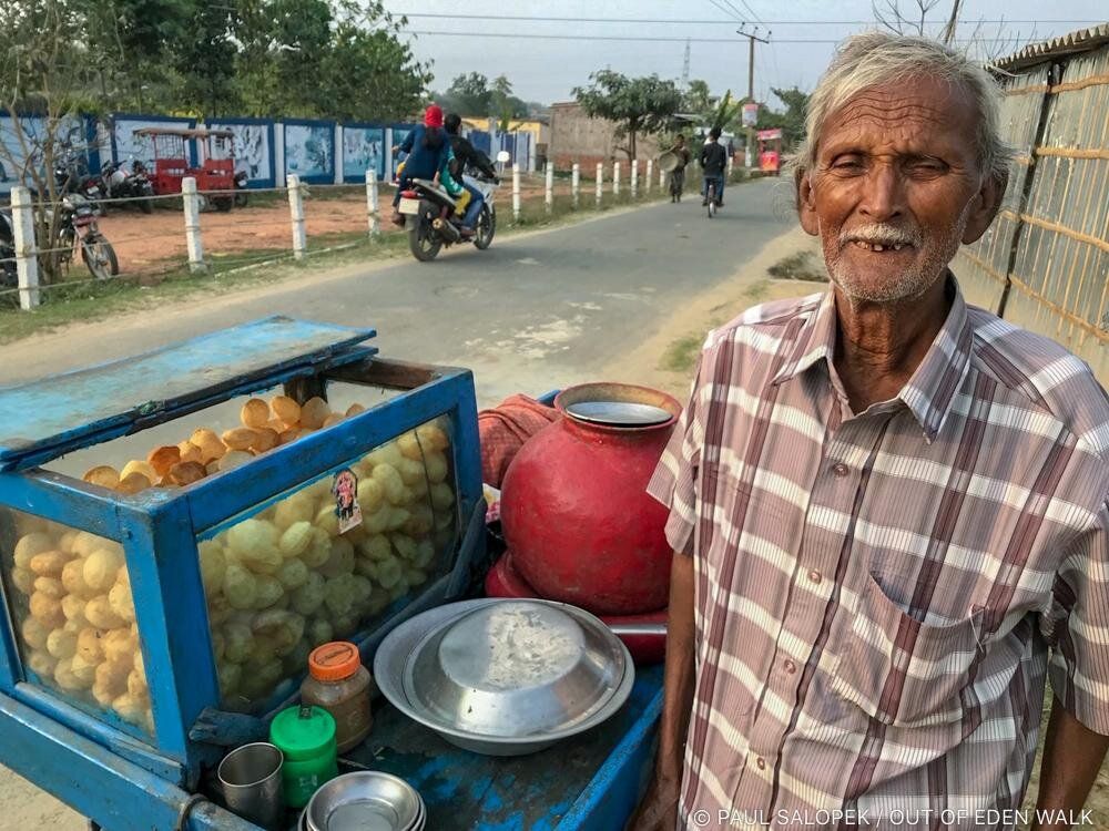 He sold pani puri from a pushcart. He swept his arms to encompass the entire horizons: his world. He wanted his photo taken. Near Purnea, Bihar, India. Image by Paul Salopek. India, 2019.