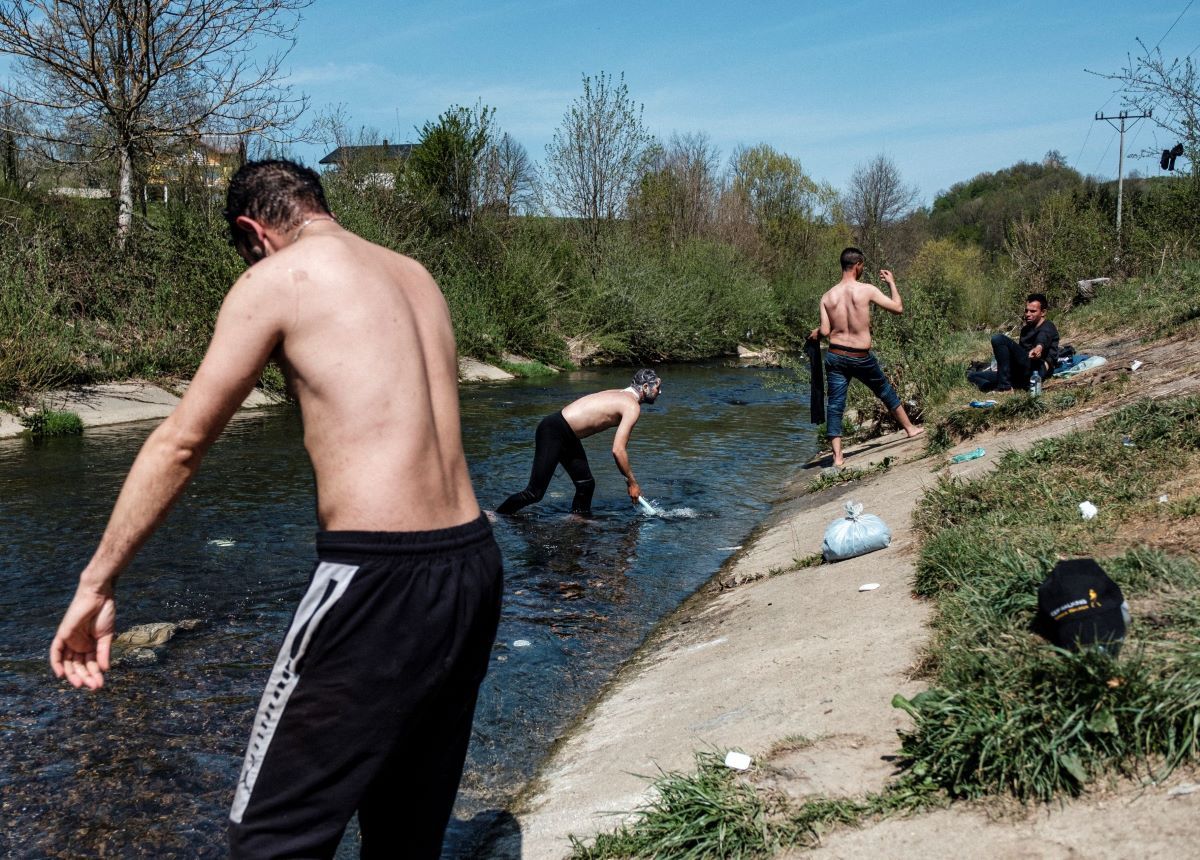 Velika Kladusa - Bosnia and Herzegovina: A group of the people on the move is seen washing their clothes and bathing in a small and polluted stream behind the abandoned factory where they built a makeshift, temporary settlement. Due to the lack of imigration centers they are forced to live outdoors and squat in inhumane conditions without access to clean water, health services and food. Image by Ziyah Gafic. Bosnia-Herzegovina, 2020.

