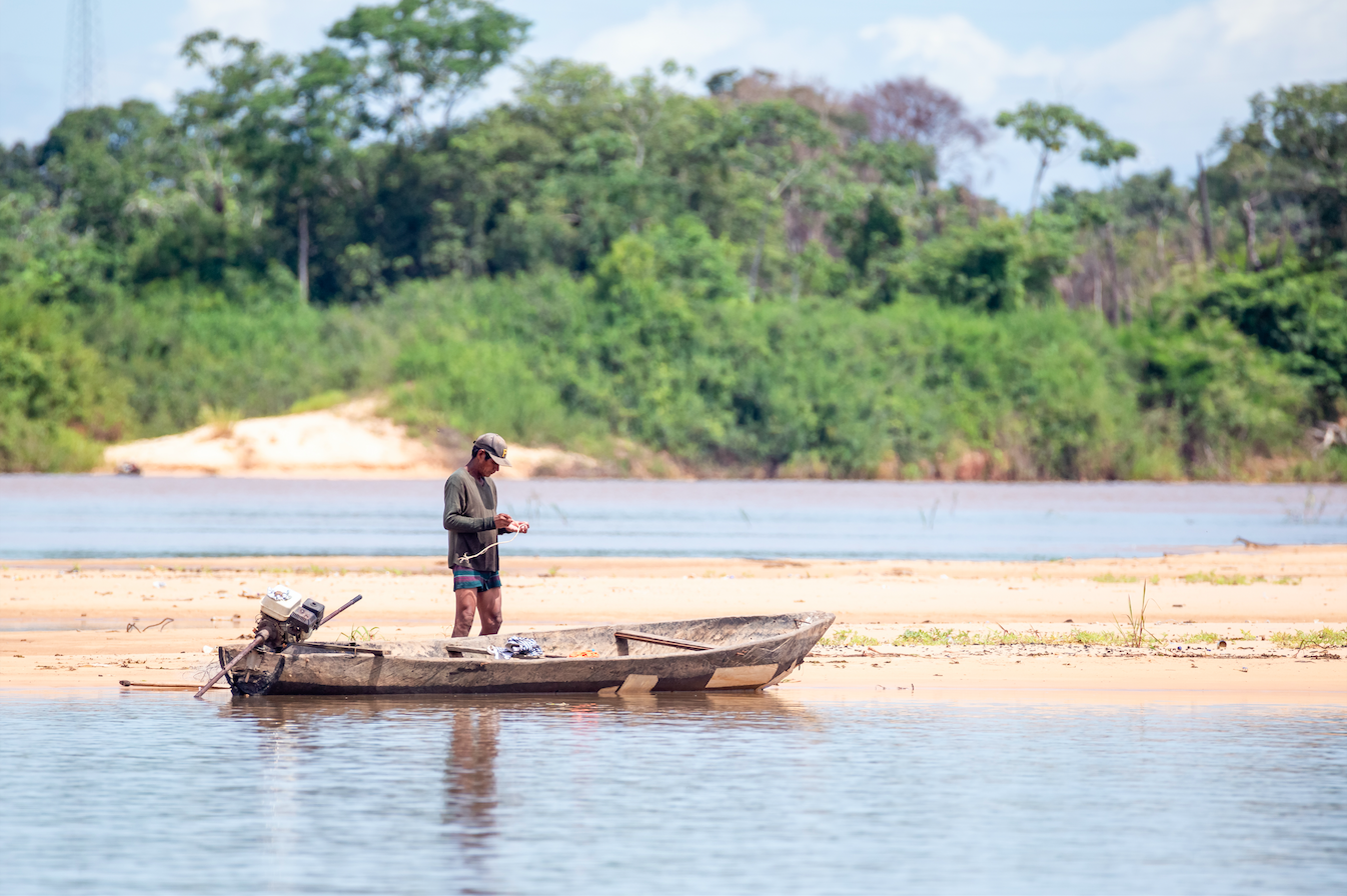A man from a traditional Indigenous population preparing his boat and tools on the Araguaia river waters in Santa Terezinha, Mato Grosso. Image by JH Bispo/Shutterstock. Brazil, 2019.