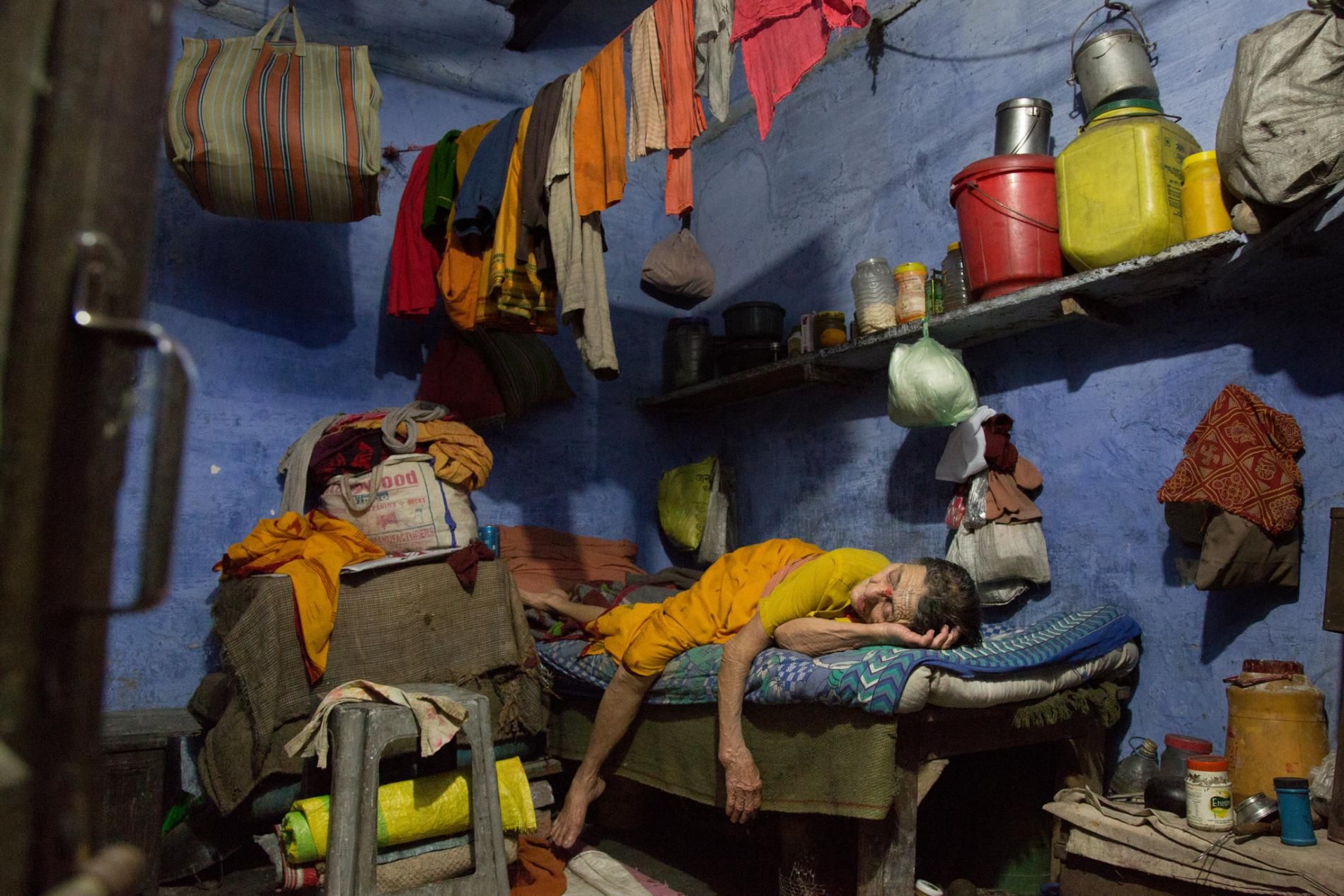 A widow’s belongings surround her in a Varanasi ashram that for generations has taken in women from Nepal. Usually run by religious charities or social-aid groups, widows’ shelters in temple cities offer a roof overhead, a surface to sleep on, and enough food to keep a lean woman alive. Women who outlive their husbands are often seen at home as tainted and burdensome, so shelters also provide an escape from hostile relatives. Image by Amy Tensing. India, 2016