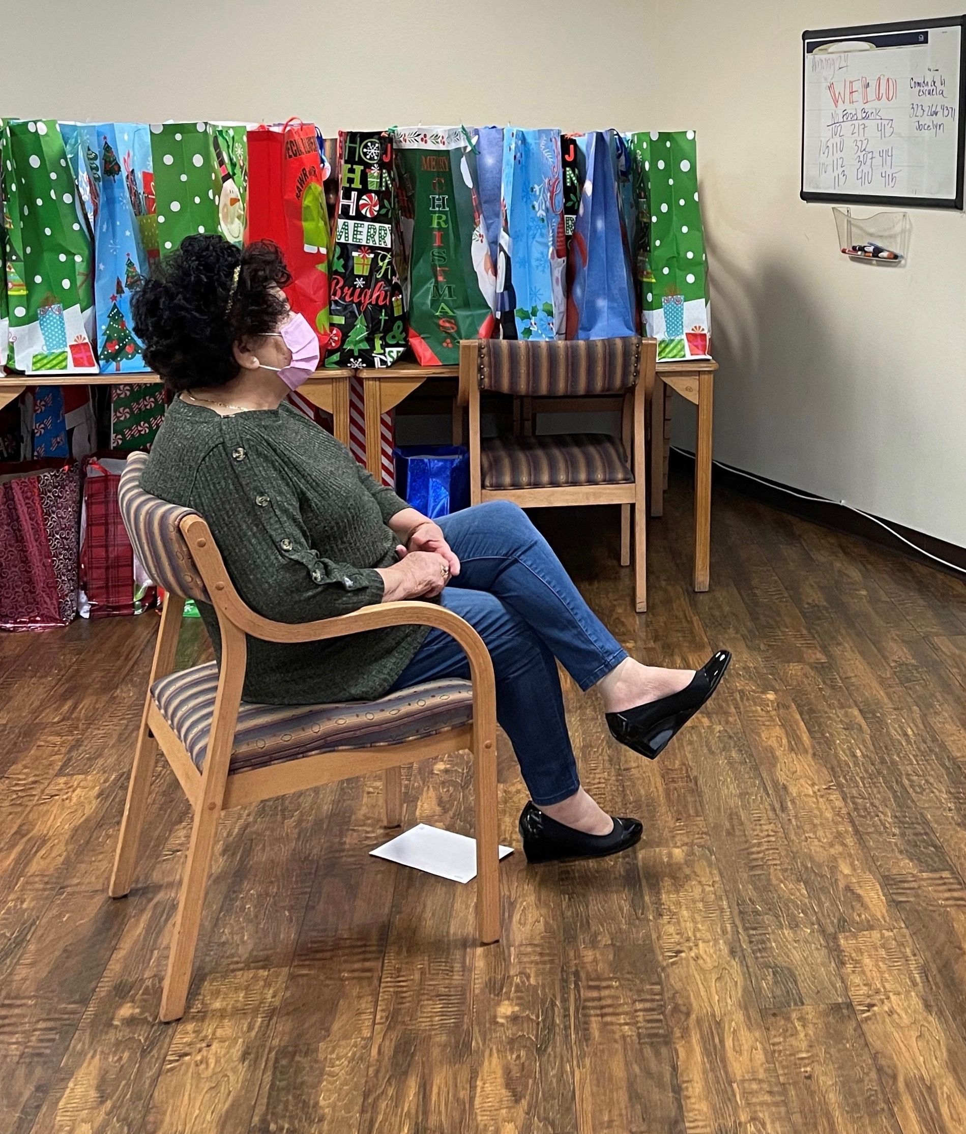 Mirna Cortez participates in a Zoom call in her building's community room, surrounded by holiday donations for seniors at the Retirement Housing Foundation. Image courtesy of Michelle Ornelas. United States, 2020.