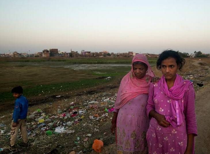 Poison everywhere: Kausar, 16, along with her mother Haseena, stands next to one of the solar evaporation ponds Union Carbide left behind in Bhopal. Kausar has low IQ and used to attend a special school until last year. The toxic waste from the factory site piped into three such huge ponds were leaking into the soil and groundwater. Image by Rohit Jain. India, 2018. 