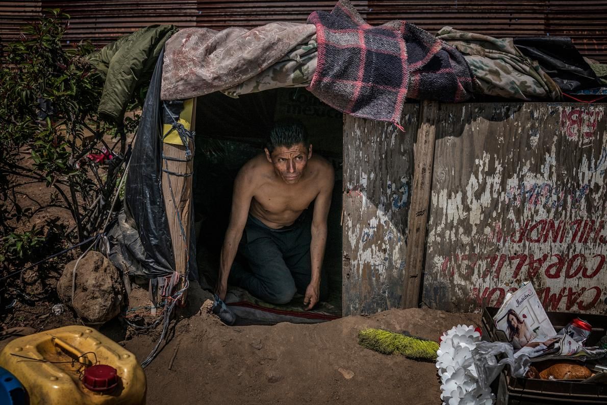 A U.S. deportee lives in a makeshift shelter atop a desolate hilltop mesa east of the Pacific Ocean beside U.S.-Mexico border wall. The man, who declined to give his real name, said he occasionally earns five dollars a day collecting shopping carts for a nearby supermarket and lives atop this hill because he feels safe. Image by James Whitlow Delano. Mexico, 2017.