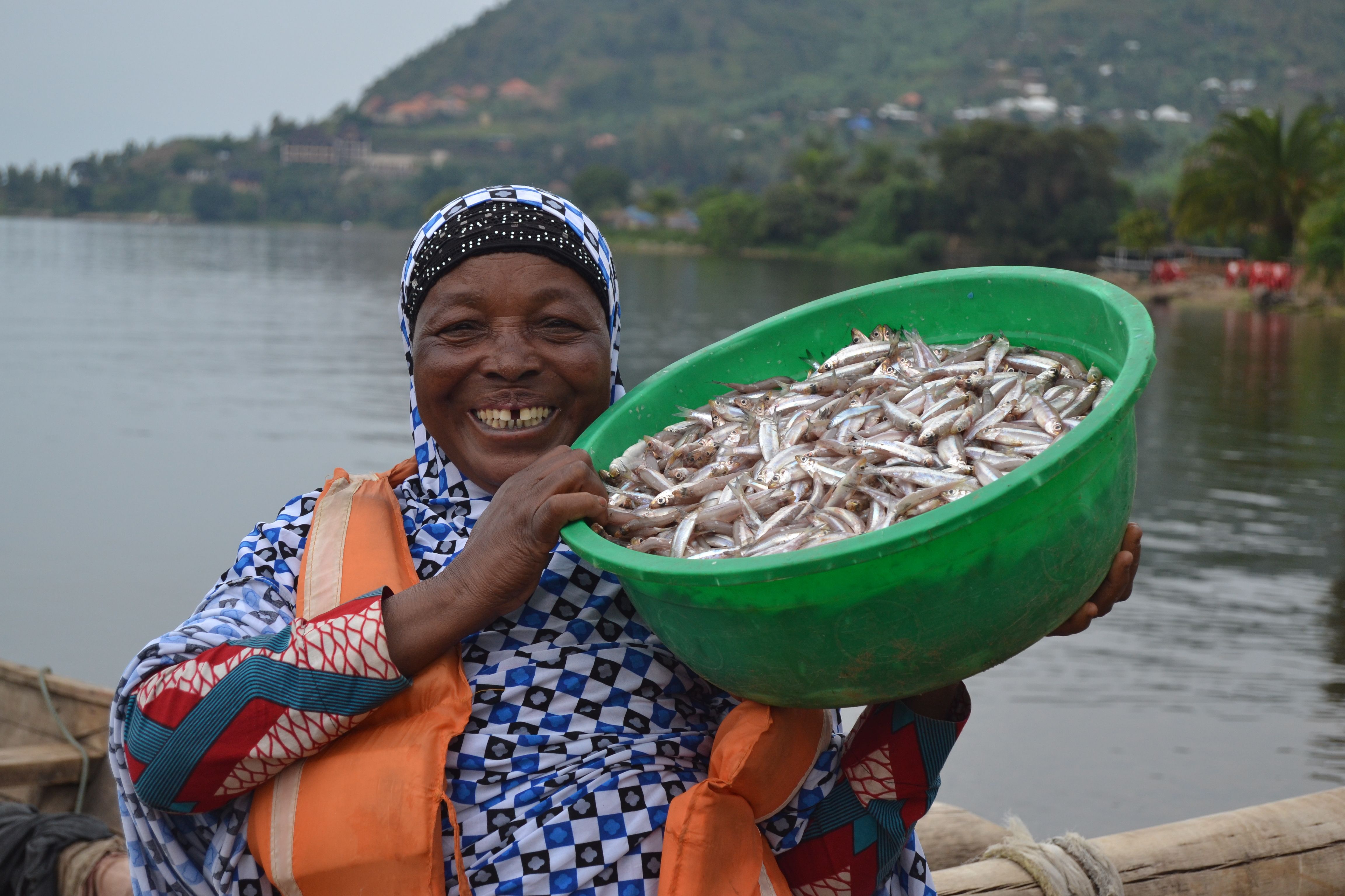 Sauda Mukamusoni, 62, poses with a bucket a fish that members of the COOPPAVI fishing cooperative caught overnight on Lake Kivu. Image by Cammie Behnke. Rwanda, 2018.