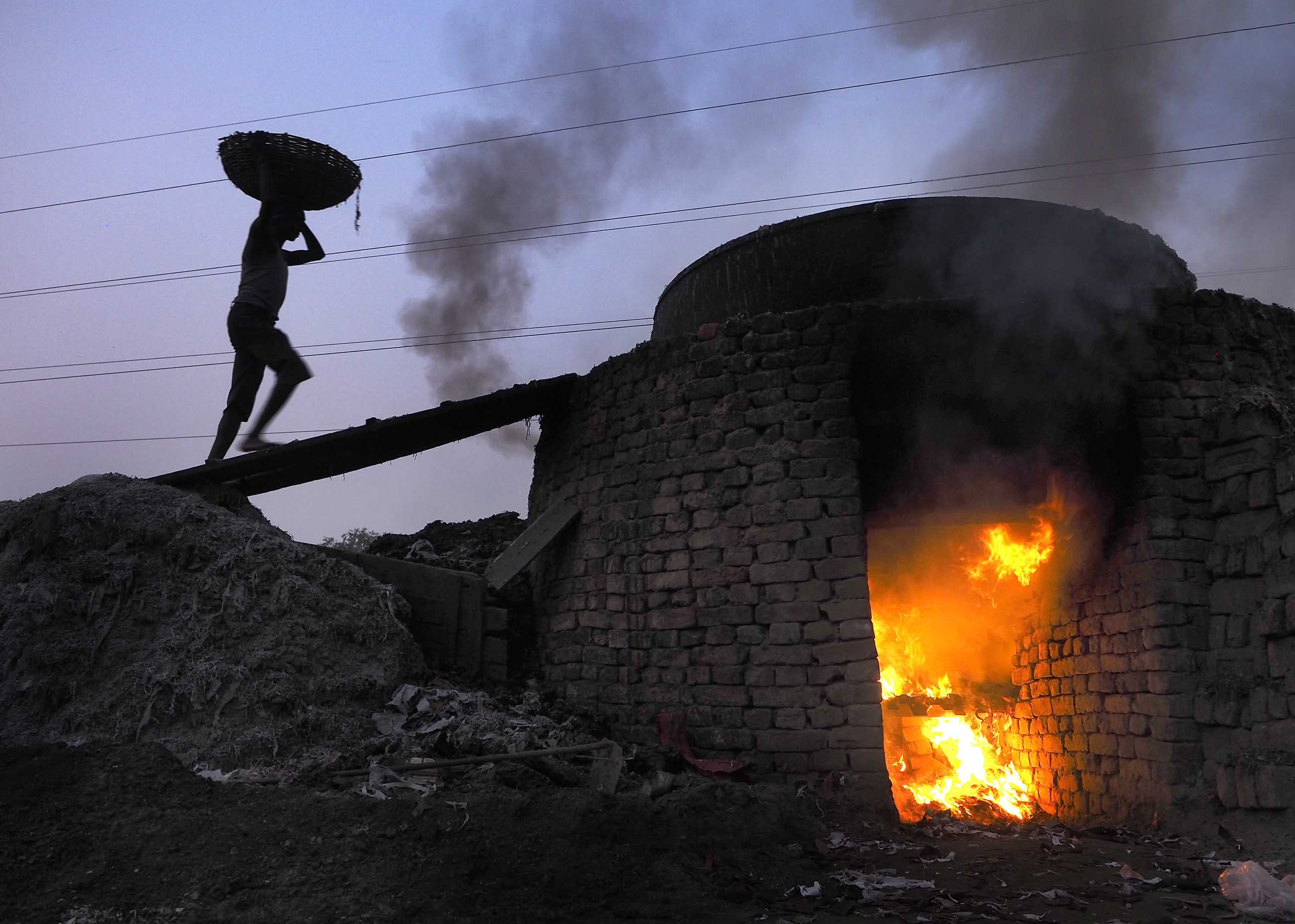 Primitive factories boil leather scraps to make glue. Here, a worker carries a basket of scraps to an enormous cauldron atop a brick oven at a glue factory near the Kolkata Leather Complex in India. Image by Larry C. Price. Bangladesh, 2016.