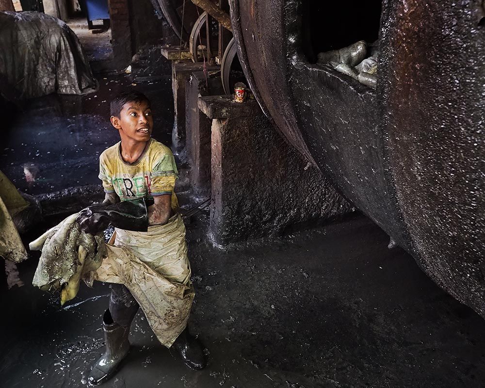 Teenagers work alongside men in some of the most dangerous tannery jobs. Bahadur tosses goat hides into a large drum full of chromium sulfate and other chemicals. Image by Larry C. Price. Bangladesh, 2016.