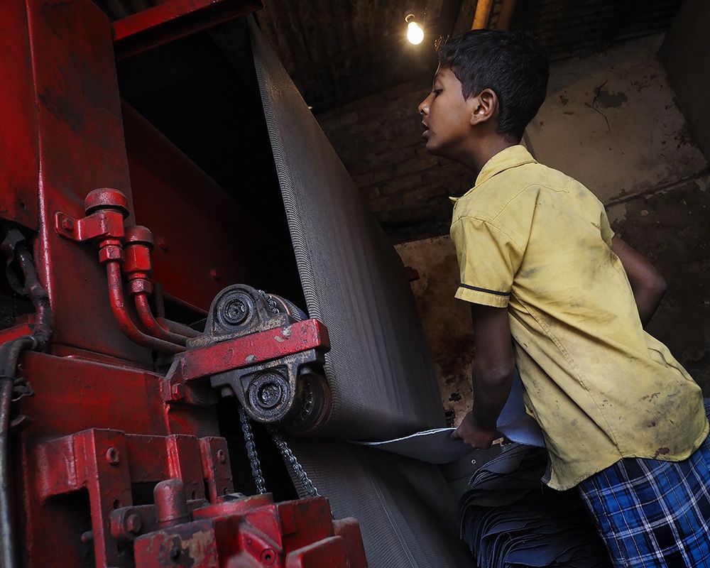 Inside the Hazaribagh tanneries, child workers are also exposed to hazardous machinery. Here, a 10-year-old boy named Joey pulls leather from a smoothing machine. Image by Larry C. Price. Bangladesh, 2016.