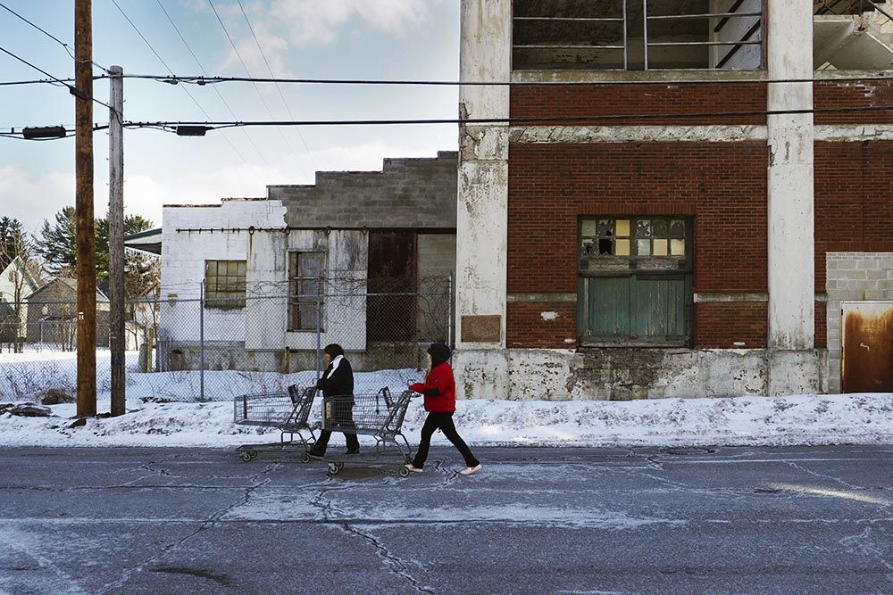 Women push shopping carts past the former Surpass Leather Company, one of several shuttered tanneries in Gloversville. Image by Larry C. Price. United States, 2016.