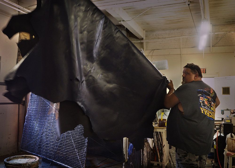 Brent Heroth, owner of Brooklynn Custom Leather Works, hangs a freshly painted piece of leather. His Gloversville, New York, shop specializes in applying custom finishes to tanned leather. Image by Larry C. Price. United States, 2016.