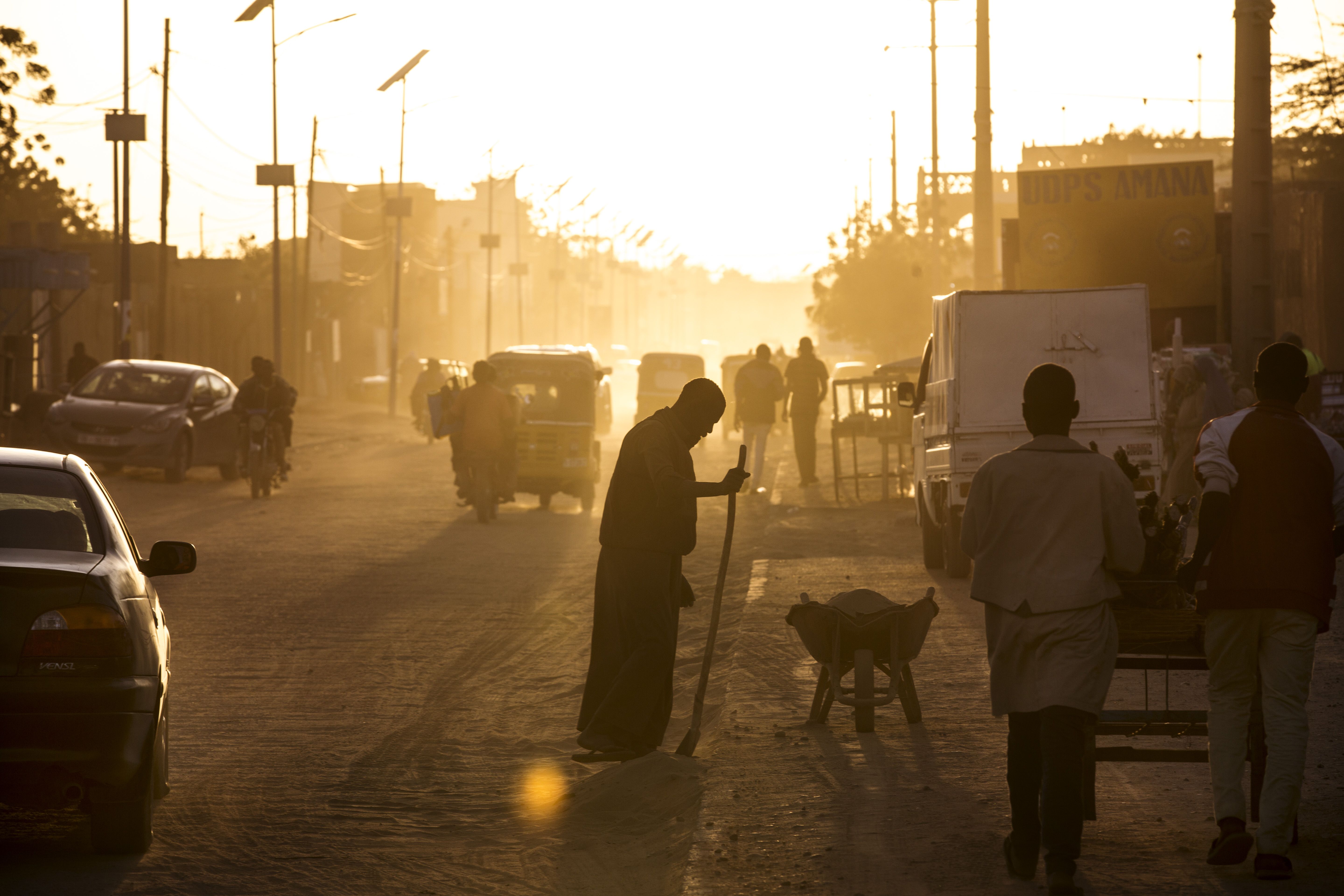 A man sweeps dust off the street at dusk in Agadez, Niger, January 16, 2018. Image by Joe Penney. Niger, 2018.