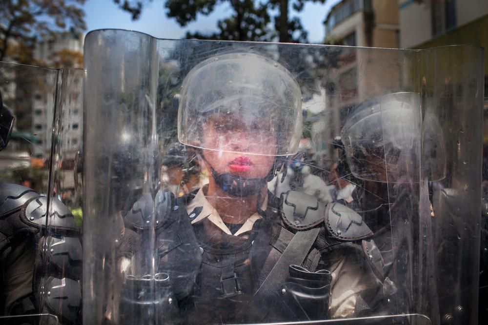 A National Police officer behind a riot shield is pushed backward by a crush of demonstrators during the March of the Empty Pots in Caracas in 2014, which coincided with International Women’s Day. Image by Natalie Keyssar. Venezuela, 2014.