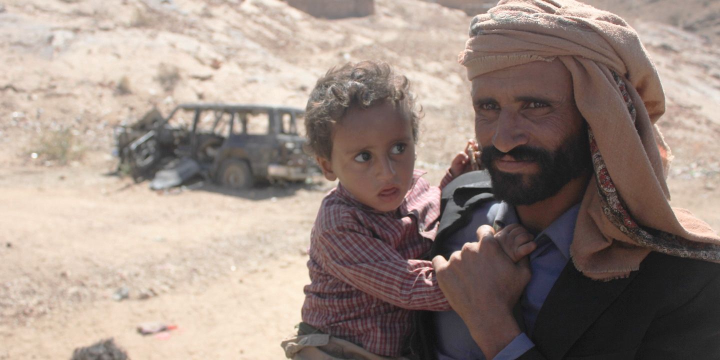 Mabkhout Ali al Ameri stands with his 18-month-old son, Mohammed, in the village of al Ghayil in Yemen’s al Bayda province. Mabkhout’s wife, Fatim Saleh Mohsen, was shot in the back of the head by helicopter gunship fire as she fled with Mohammed in her arms during a U.S. raid. Image courtesy of The Intercept. Yemen, 2017.