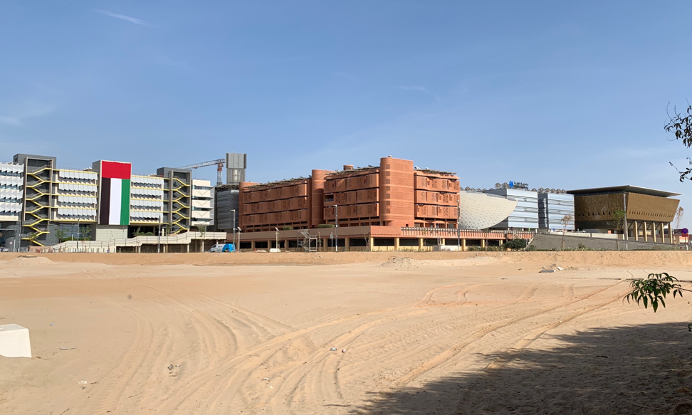 View from the road of Masdar City’s completed buildings. From left to right: Siemens Middle East Headquarters, Khalifa University Residential Building, Knowledge Centre, Multipurpose Khalifa University Building, and Multi-Use Hall. Image by Anna Gleason. United Arab Emirates, 2019.