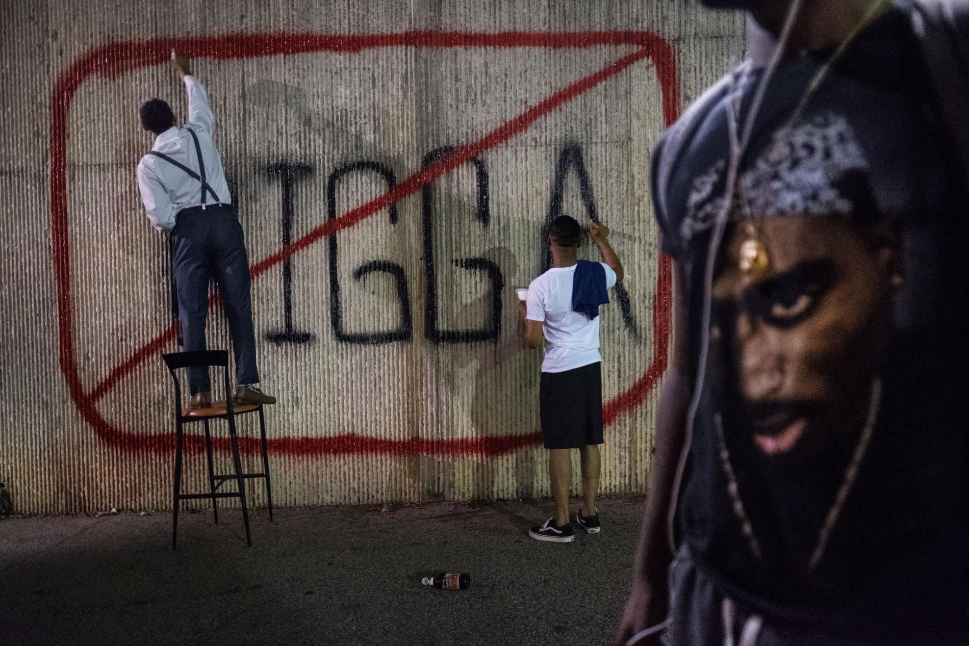 Morehouse College student government leaders John Cooper and Kamren Rollins paint a sign on campus to stimulate discussion about the N-word. Another student passes by wearing a T-shirt with an image of the late rap artist Tupac Shakur, who used the term liberally in his lyrics. Image by Radcliffe "Ruddy" Roye. United States, 2017.
