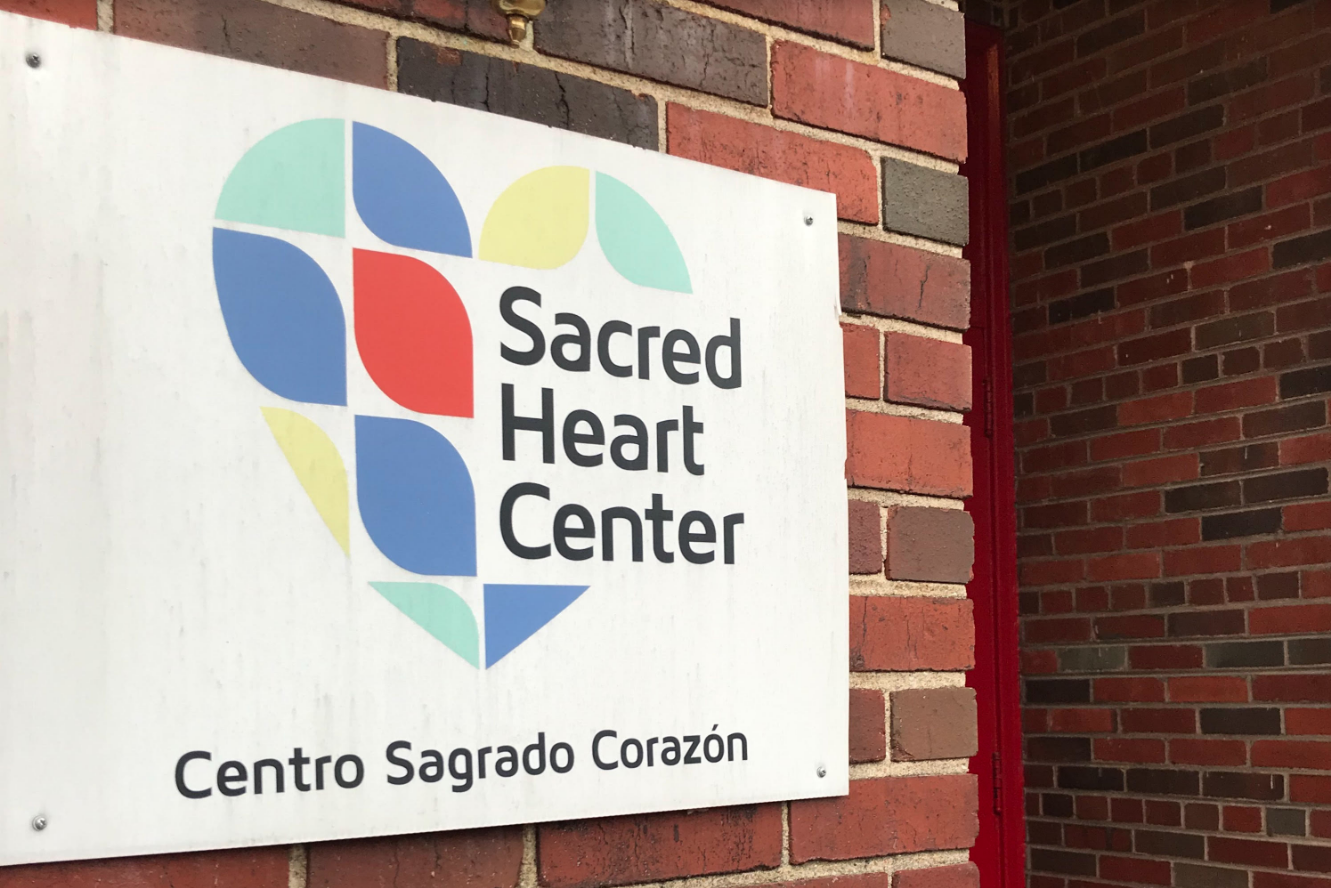 A bilingual sign at the Sacred Heart Center, welcoming all those who enter the community building. Image by Jack Sims. United States, 2019.