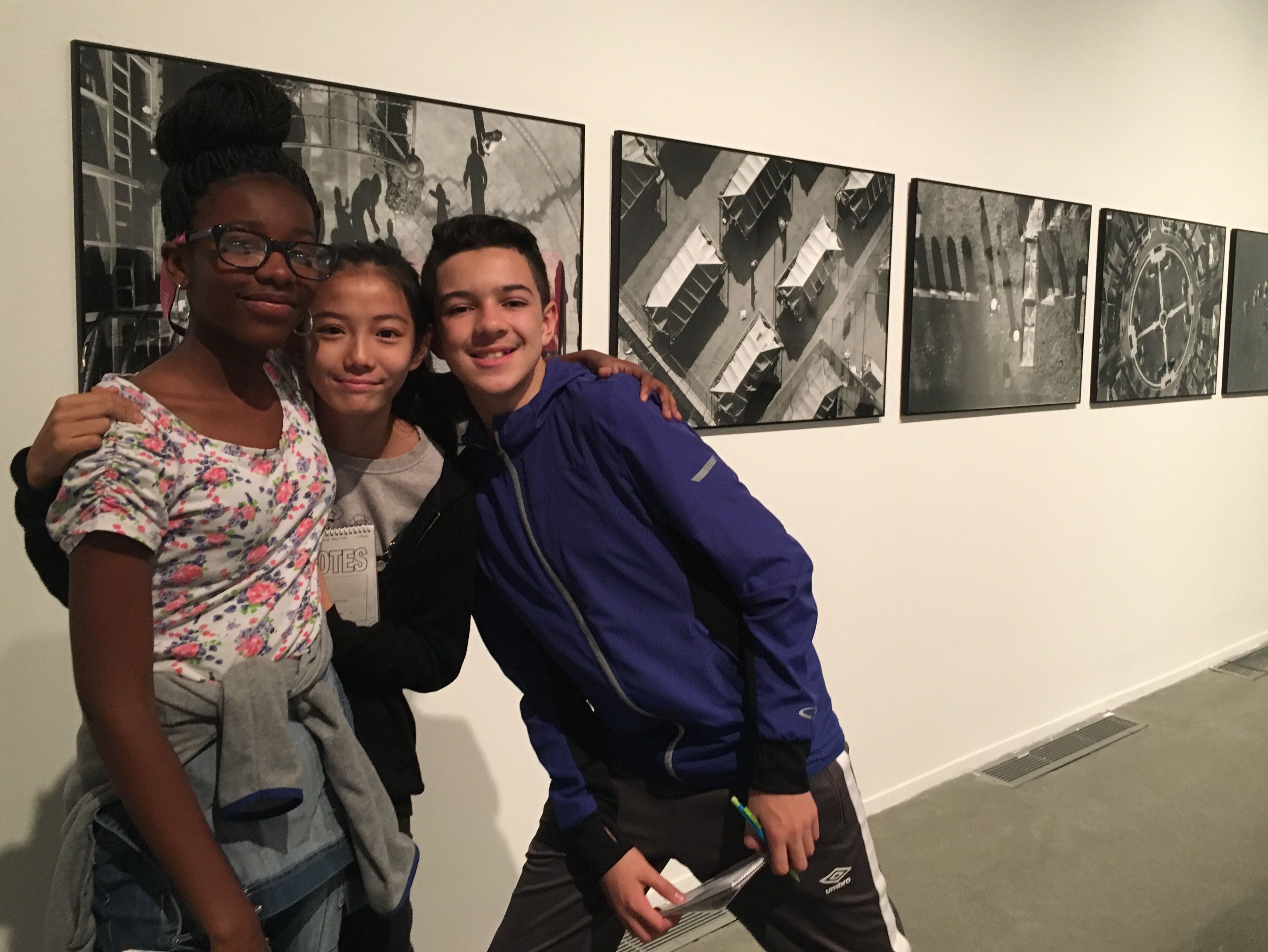 Students pose with photos taken by Tomas van Houtryve in the "Dispatches" exhibition. Image by Diana Greene. United States, 2016.