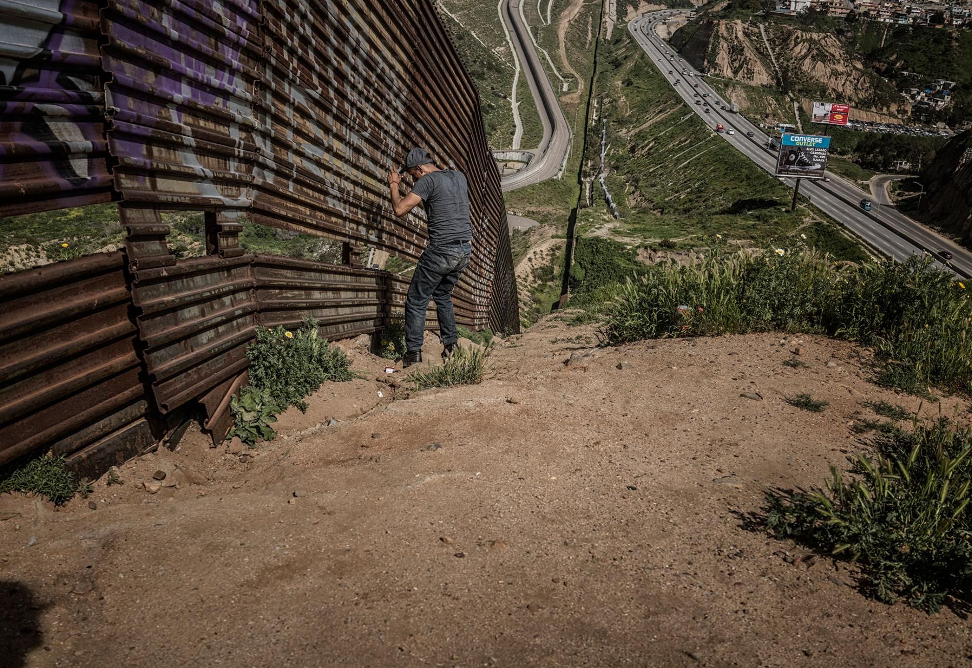  A man, likely a human trafficker known as a "coyote," studies a vulnerable stretch of border wall in Tijuana. There is a gap in one area of wall, offering an opening to traffickers of people and drugs. Image by James Whitlow Delano. Mexico, 2017.