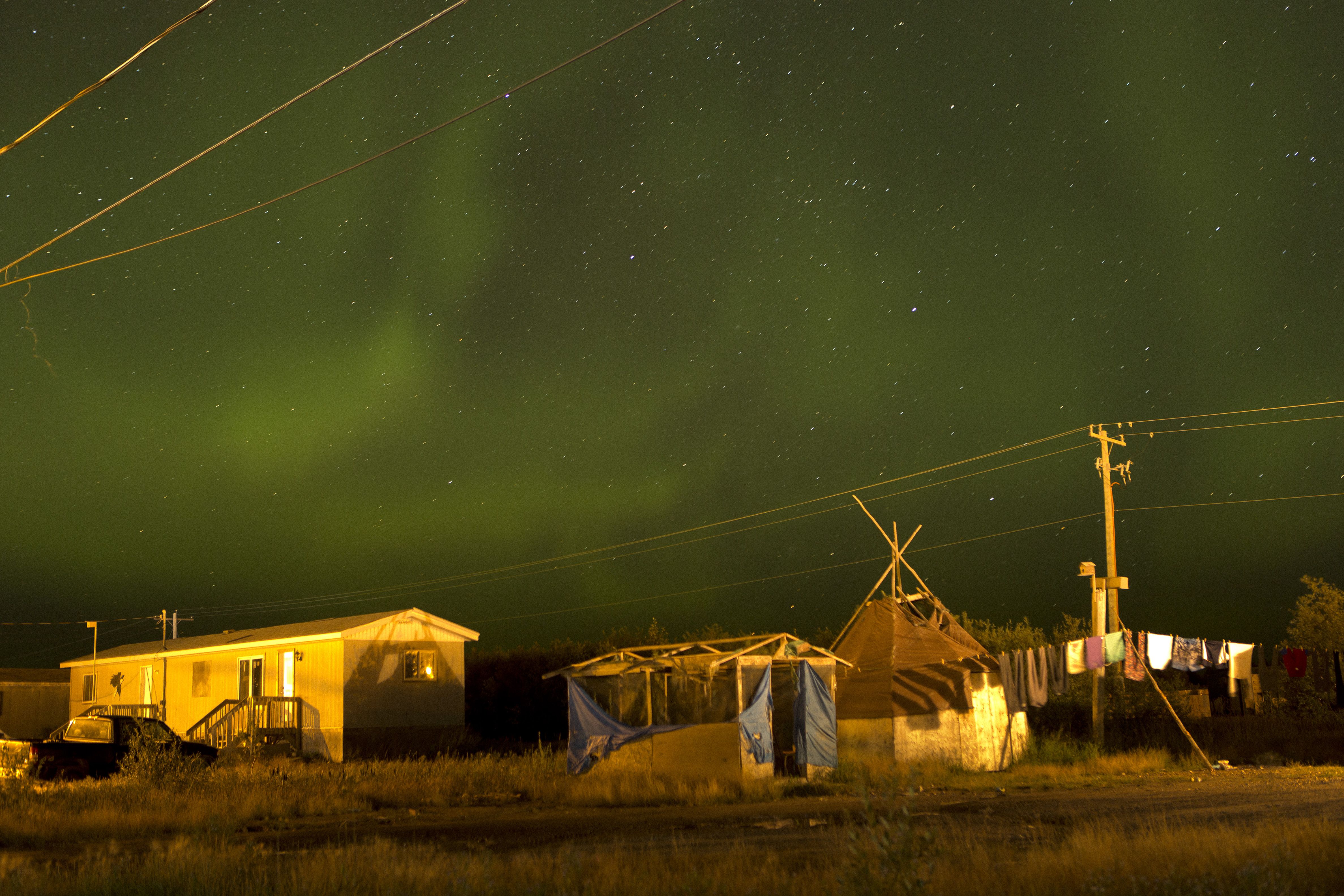 Attawapiskat, Ontario, Canada. The Northern lights, almost overpowering in their physical beauty, fill the night sky over Attawapiskat. Cree legends state that the lights are spirits of the ancestors celebrating life and showing the living that they are all part of creation. Their dancing forms a laneway for the souls as they travel to the next realm. It is said that when Cree are living the right way and conducting ceremonies and dances, the spirits of Cree ancestors celebrate in the heavens. Image by David Maurice Smith. Canada, 2016.