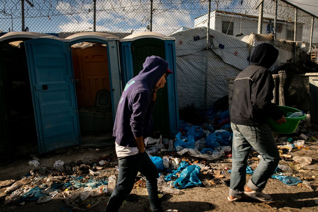 Dumpsters overflowing with garbage and unkempt porta-potties line the walkways of Moria in Lesbos. Image by Maranie Staab. Greece, 2020.
