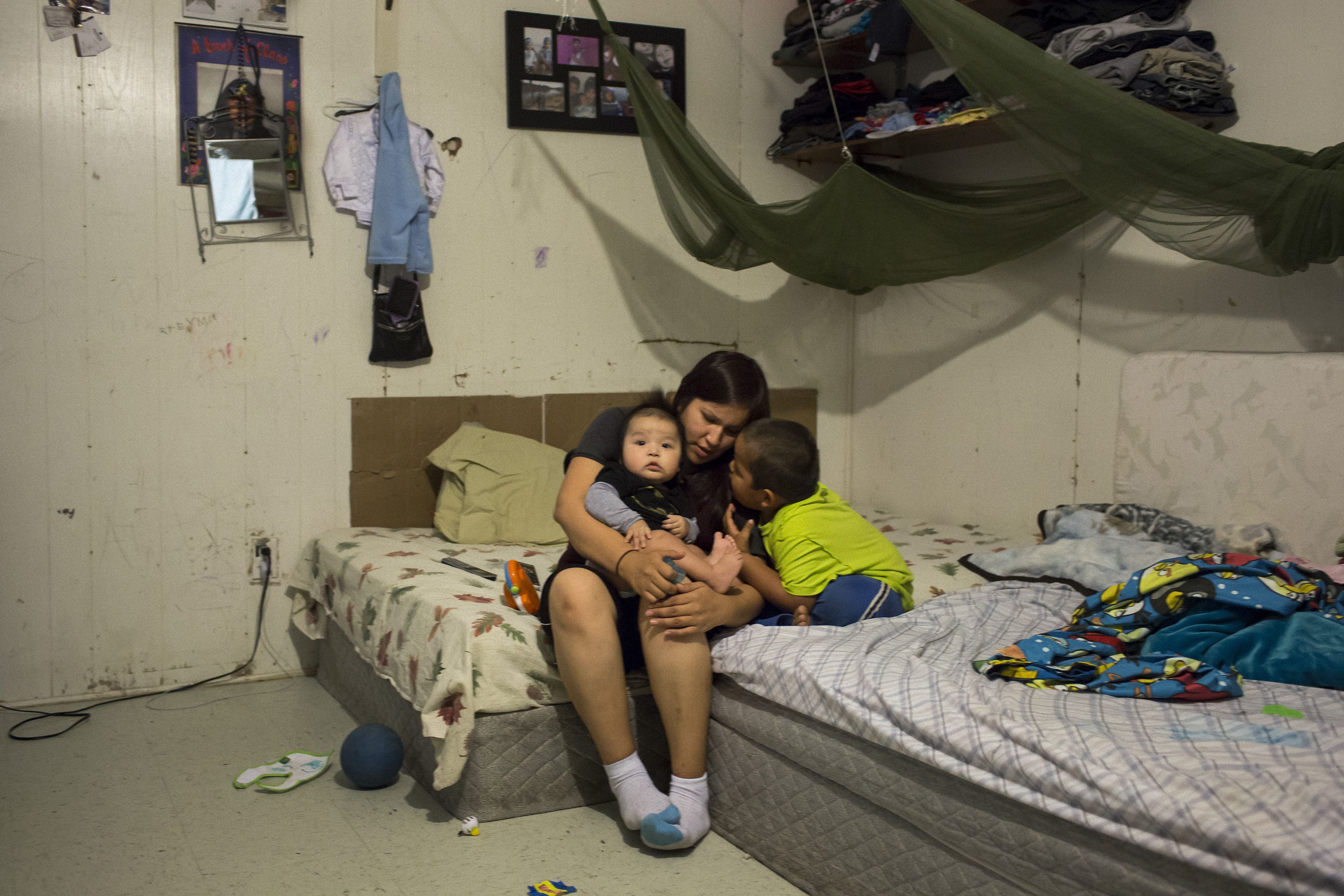 Twenty-five-year-old Martina Koosees with her six-month-old son Korey Koosees and son Dyson Koosees, 4, in the single room dwelling where they live. The pressures of a chronic housing shortage leave families forced to live in very cramped conditions, amplifying many of the stresses the encounter in their lives. As one member of the community put it, “We have so many shortages for housing and social programs in our communities. Families are stressed out. It is a manifestation of an ongoing colonialism.” Image by David Maurice Smith. Canada, 2016.