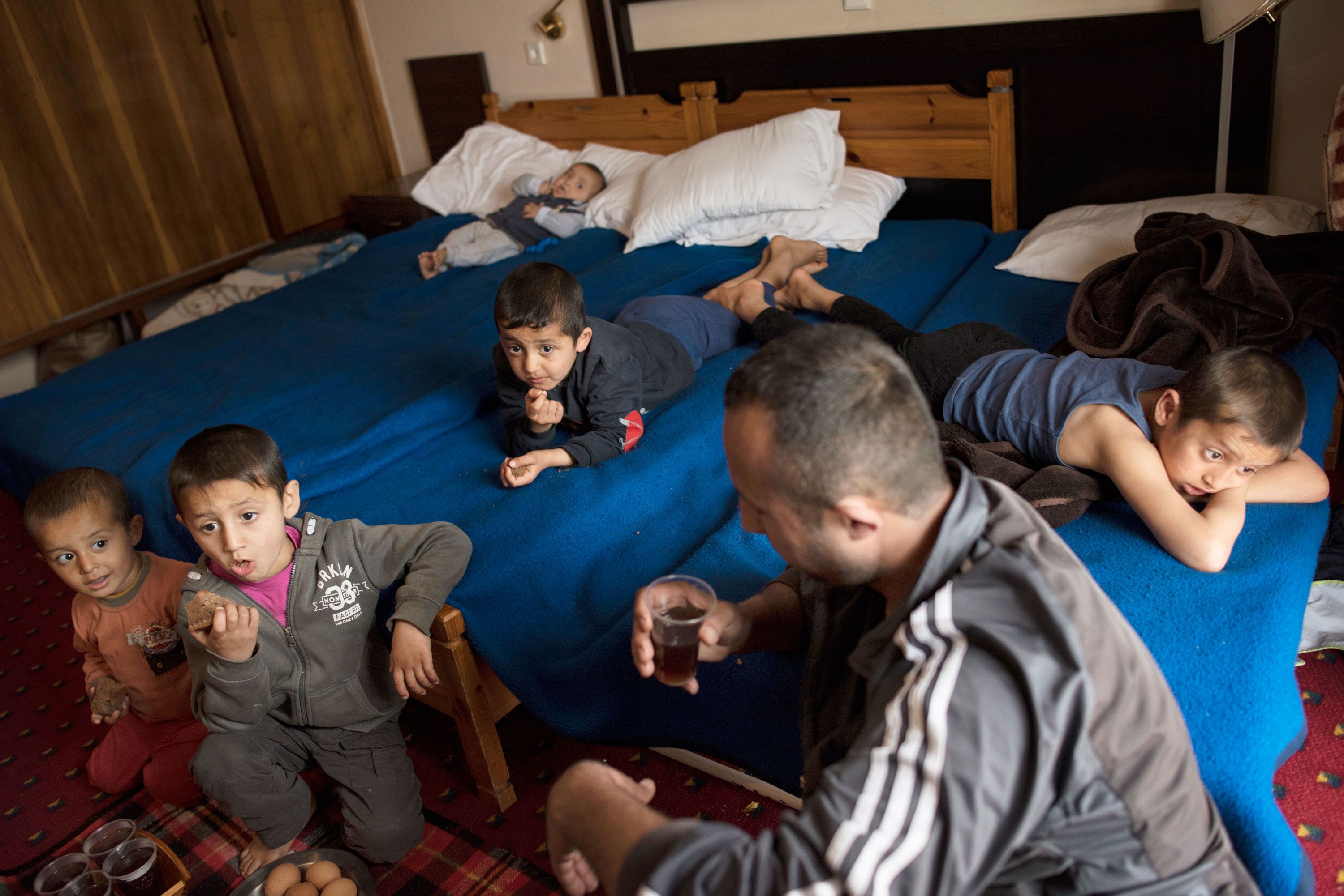 Minhel drinks tea while his children watch television in a hotel in Kastoria, Greece, near the Albanian border. Image by Lynsey Addario. Greece, 2017.