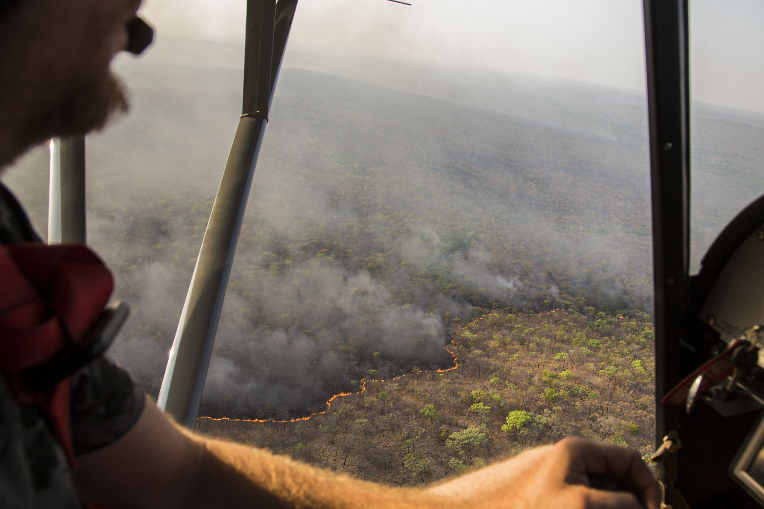Cédric Ganière flies over a bush fire on the Chinko savannah in his tiny, two-seater plane during a mission to spot cattle herders and blazes. Image by Jack Losh. Central African Republic, 2018.