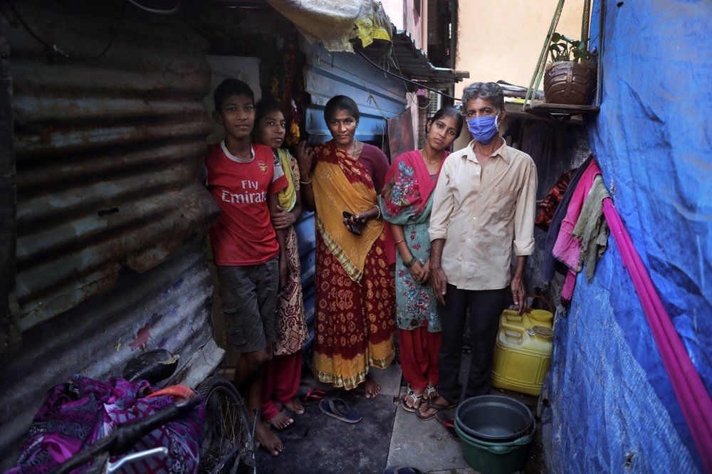 In this April 3, 2020, photo, Mina Ramesh Jakhawadiya, center, poses for a picture with her family members, son, Ritik Ramesh, left, daughters Vaijayanti Ramesh, second left, Guddi Ramesh, second right, and husband Ramesh Karsan Jakhawadiya, outside her one room house in a slum in Mumbai, India. Jakhawadiya makes a living selling cheap plastic goods with her husband on the streets of Mumbai. For her, the order means 21 days in a 6-by-9 foot room with five people, no work, a couple days of food and very less cash. As governments around the world debate ways to slow the spread of coronavirus, India has launched one of the most draconian social experiments in human history, locking down its entire population, including hundreds of millions of people who struggle to survive on a few dollars a day. Image by AP Photo/Rajesh Kumar Singh. India, 2020.