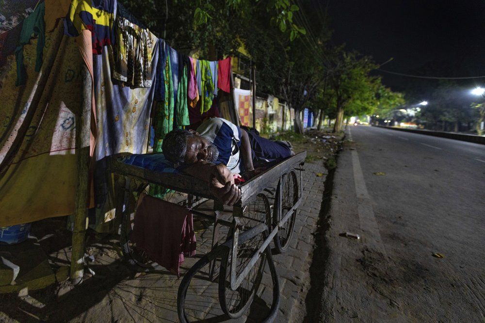 In this April 3, 2020, photo, Rajesh Dhaikar sleeps on his handcart on which he sells balloons, outside his one room house in Prayagraj, India. Dhaikar has a small balloon stall in a nearby market, selling plastic bursts of red and blue and yellow one at a time, and rarely earning more than $2.50 a day. His wife, Suneeta, makes about $20 a month cleaning homes. They have five children, ranging in age and a bank account with about $6.50 in it. India has launched one of the most draconian social experiments in human history, locking down its entire population, including hundreds of millions of people who struggle to survive on a few dollars a day. Image by AP Photo/Rajesh Kumar Singh. India, 2020.