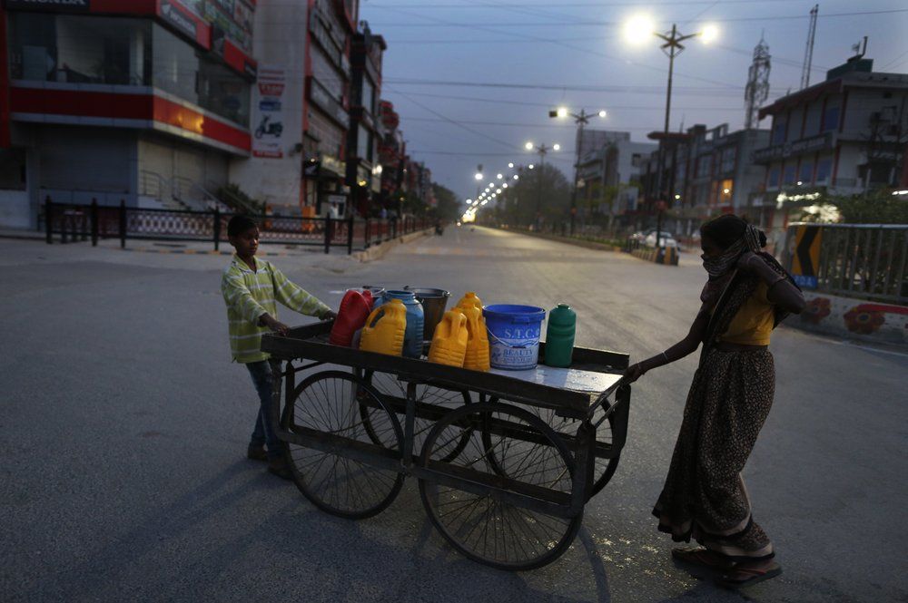 In this April 8, 2020, photo, Rajesh Dhaikar's wife Suneeta and son Deepu bring water on their hand cart for the house in Prayagraj, India. Dhaikar has a small balloon stall in a nearby market, selling plastic bursts of red and blue and yellow one at a time, and rarely earning more than $2.50 a day. His wife, Suneeta, makes about $20 a month cleaning homes. They have five children, ranging in age and a bank account with about $6.50 in it. India has launched one of the most draconian social experiments in human history, locking down its entire population, including hundreds of millions of people who struggle to survive on a few dollars a day. Image by AP Photo/Rajesh Kumar Singh. India, 2020.