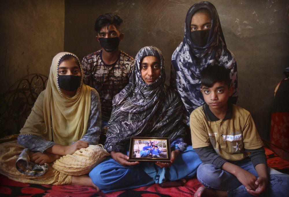 In this April 10, 2020, photo, Fatima Begum, a widow, who sells vegetables on roadside, holds the photograph of her husband as she poses for a photo with her children, sons Mohammad Eliyas, behind left, and Sameer, front right, daughters Sabina Akhtar, behind right, and Shabnam Akhtar, left, in their house on the outskirts of Jammu, India. Begum is one among the millions of workers who are part of India's par of informal economy that has been worse hit by the nationwide lockdown, pushing many like her in deeper poverty. India has launched one of the most draconian social experiments in human history, locking down its entire population, including hundreds of millions of people who struggle to survive on a few dollars a day. Image by AP Photo/Rajesh Kumar Singh. India, 2020.