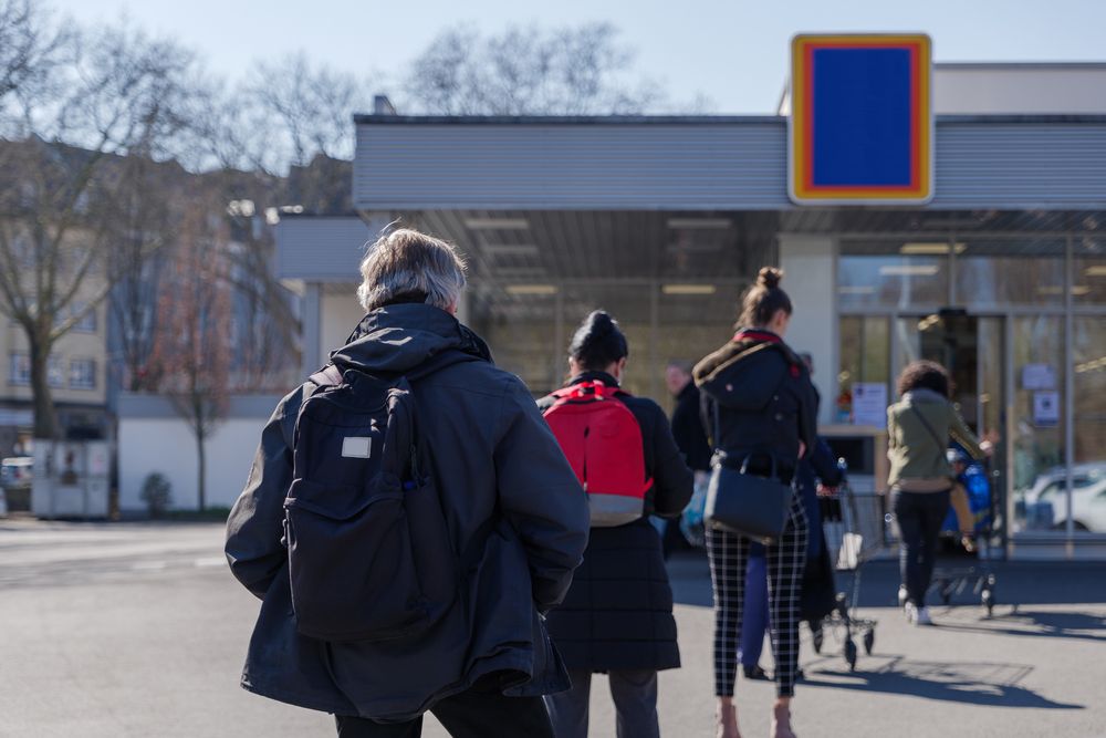European people queue on street outside supermarket during quarantine for COVID-19 virus in Düsseldorf, Germany. Image by Peeradontax / Shutterstock. Germany, 2020.