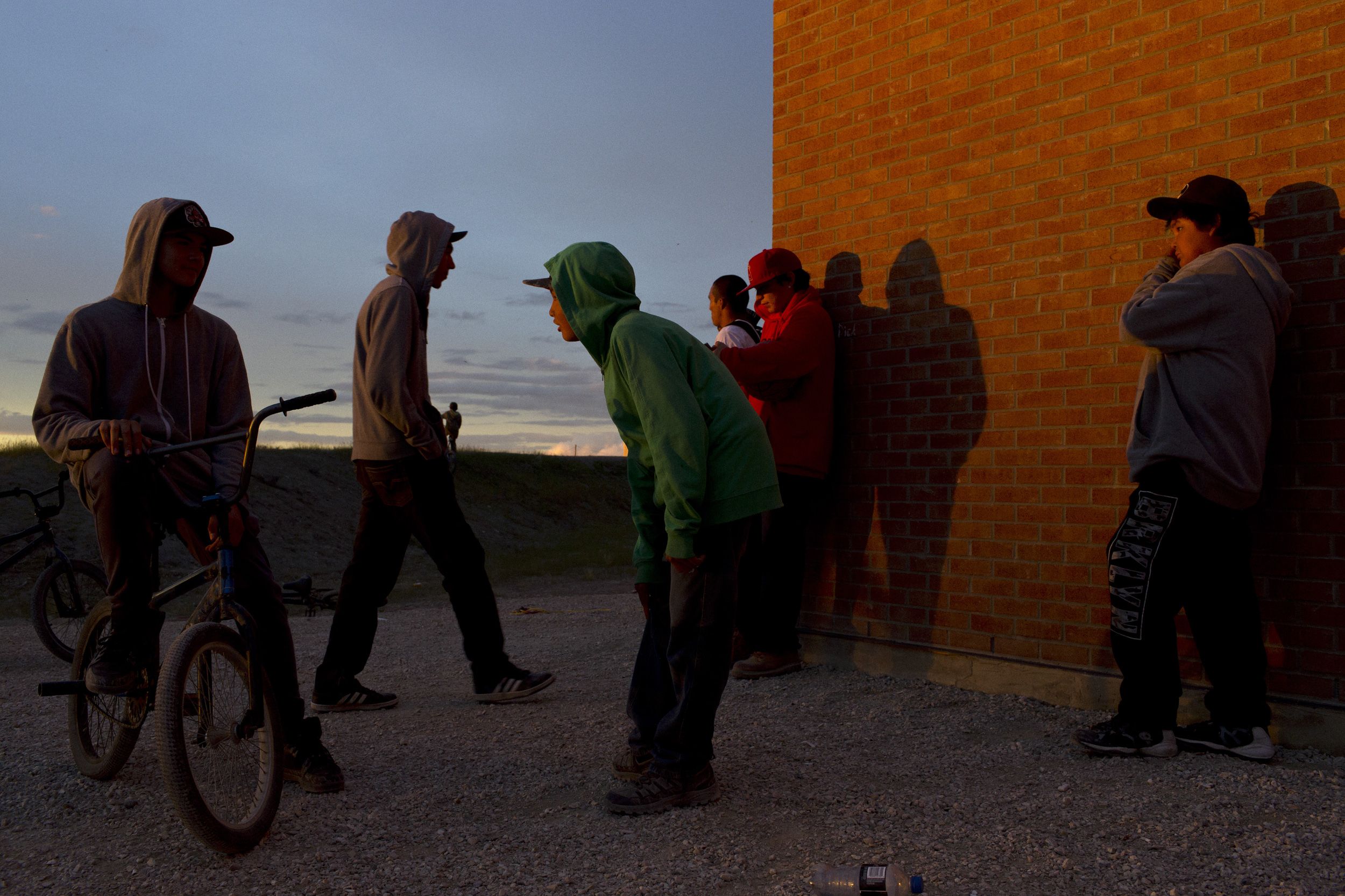 Young people gather at dusk outside the Kattawapiskak Elementary School. The suicide crisis that captured media attention in 2016 included attempts by teenagers. Image by David Maurice Smith/Oculi. Canada, 2016.