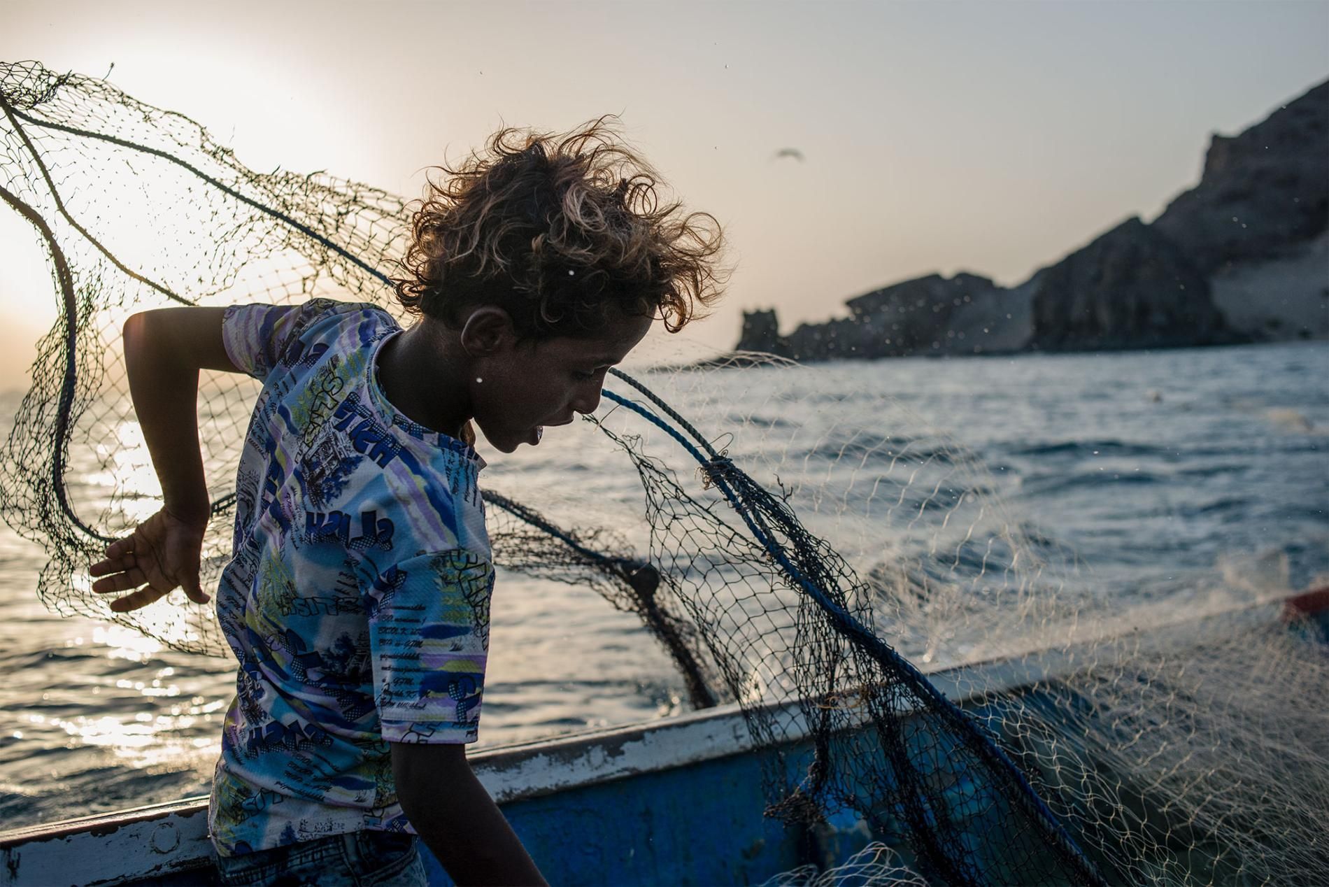 Musa throws a net into the ocean after spotting a school of fish. Image by Alex Potter. Yemen, 2018.
