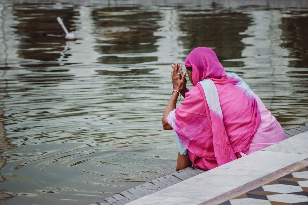 Sikh woman in pink sari dress praying at sacred pool. Image by Gabriela Rosell / Shutterstock. India, undated.