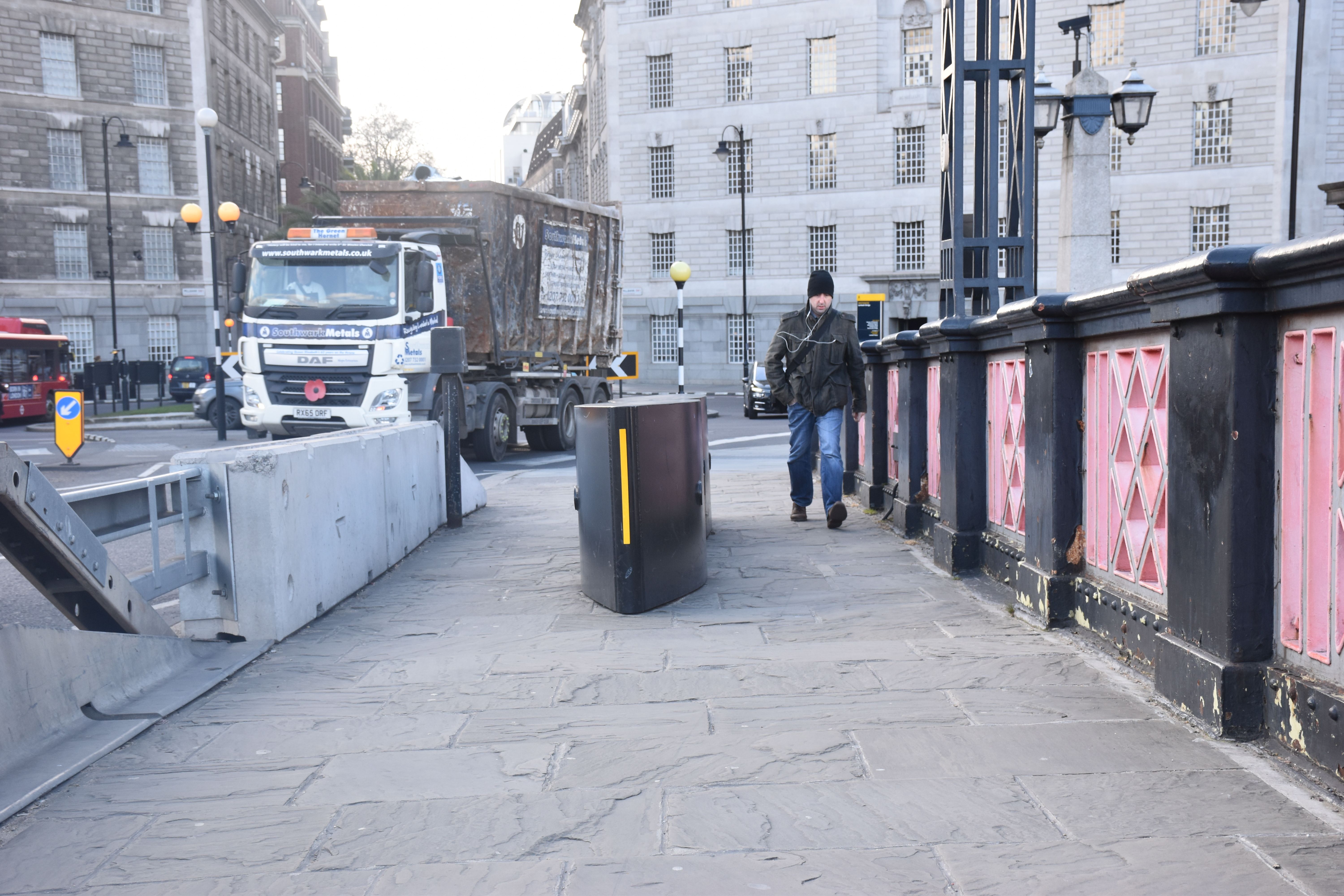 A man walks past a barricade on the Lambeth Bridge meant to stop vehicles from driving on the sidewalk. Image by Paul LeBlanc. United Kingdom, 2018.