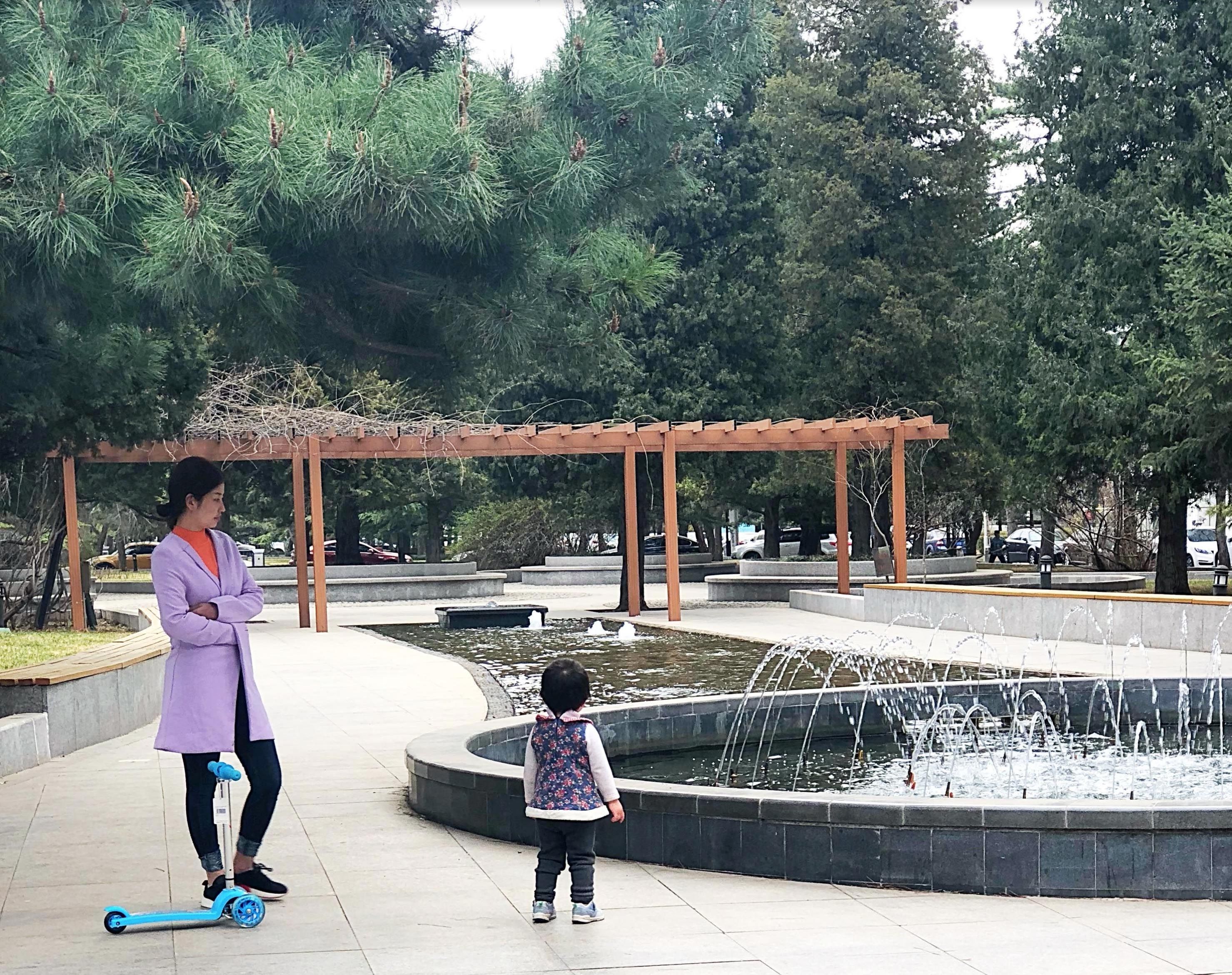 A young woman stands with her daughter in the park in front of Minzu University in Beijing. Image by Argentina Maria-Vanderhorst. China, 2018.