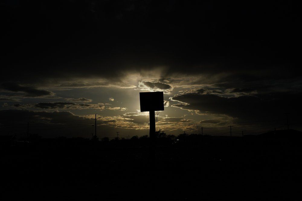 The sun sets behind a basketball hoop and backboard at Dinehdeal family compound in Tuba City, Ariz., on the Navajo reservation on April 20, 2020. The reservation has some of the highest rates of coronavirus in the country. If Navajos are susceptible to the virus' spread in part because they are so closely knit, that's also how many believe they will beat it. Image by AP Photo/Carolyn Kaster. United States, 2020.