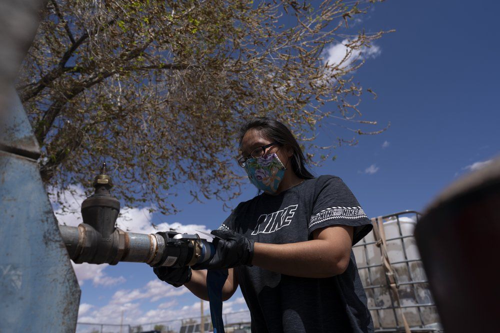 Raynelle Hoskie attaches a hose to a water pump to fill tanks in her truck outside a tribal office on the Navajo reservation in Tuba City, Ariz., on April 20, 2020. Hoskie is hauling water back to her home where she lives with her extended family. The reservation has some of the highest rates of coronavirus in the country. If Navajos are susceptible to the virus' spread in part because they are so closely knit, that's also how many believe they will beat it. Image by AP Photo/Carolyn Kaster. United States, 2020.