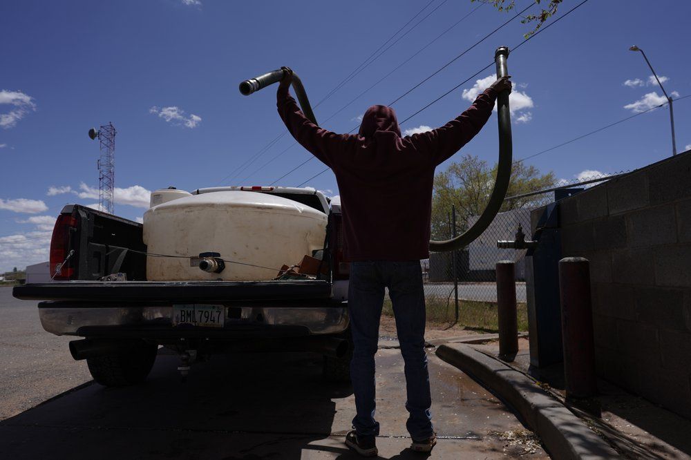 A man runs a hose from a water pump to fill a water tank in the back of a pickup truck outside a tribal office on the Navajo reservation in Tuba City, Ariz., on April 20, 2020. The reservation has some of the highest rates of coronavirus in the country. If Navajos are susceptible to the virus' spread in part because they are so closely knit, that's also how many believe they will beat it. Image by AP Photo/Carolyn Kaster. United States, 2020.