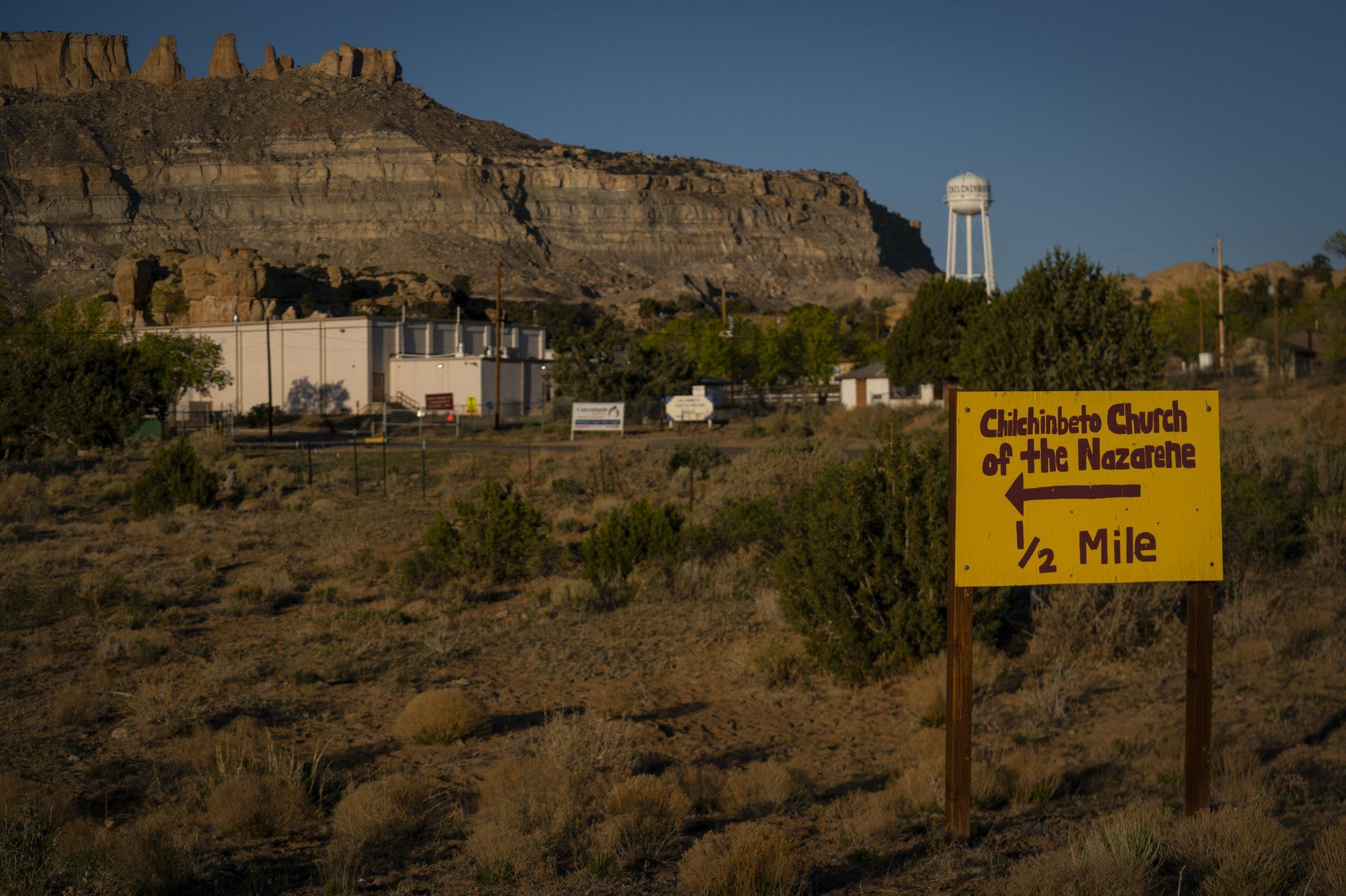A hand-painted sign points the way to the Chilchinbeto Church of the Nazarene in Chilchinbeto, Ariz., on the Navajo reservation at sunrise on Sunday, April 19, 2020. The Navajo reservation has some of the highest rates of coronavirus in the country. If Navajos are susceptible to the virus' spread in part because they are so closely knit, that's also how many believe they will beat it. Image by AP Photo/Carolyn Kaster. United States, 2020.