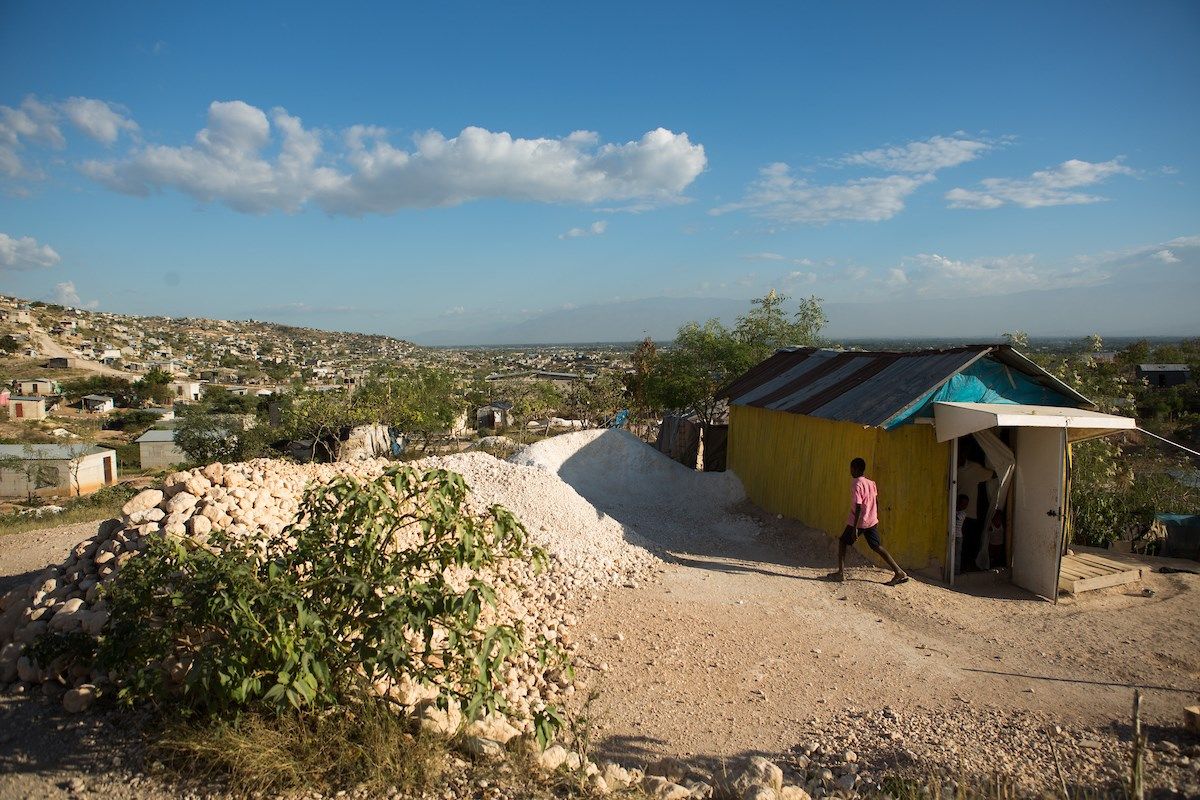 A boy walks past a home in the Canaan I section of the Canaan settlement, just outside of Port-au-Prince, Haiti. Image by Allison Shelley. Haiti, 2018.