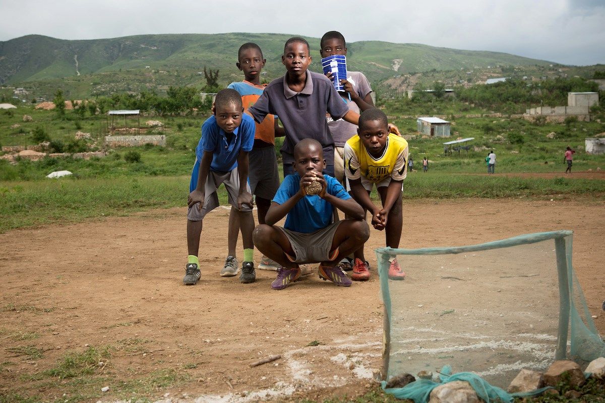 Boys pose for a photo with their handmade ball during a pickup game in the Canaan I section of Canaan. The community has gone to great lengths to protect the choice piece of land that the pitch is on — a rare flat spot in a hilly region — hoping one day to build a soccer stadium here. Community leaders have helped newcomers who have tried to claim the site to find plots farther up the hill. Image by Allison Shelley. Haiti, 2018.